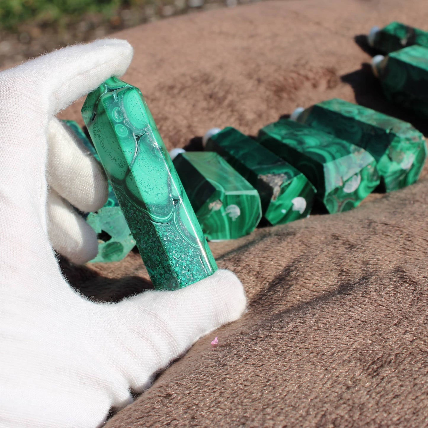 Hand holding a green Malachite tower from the Malachite tower collection on a textured surface