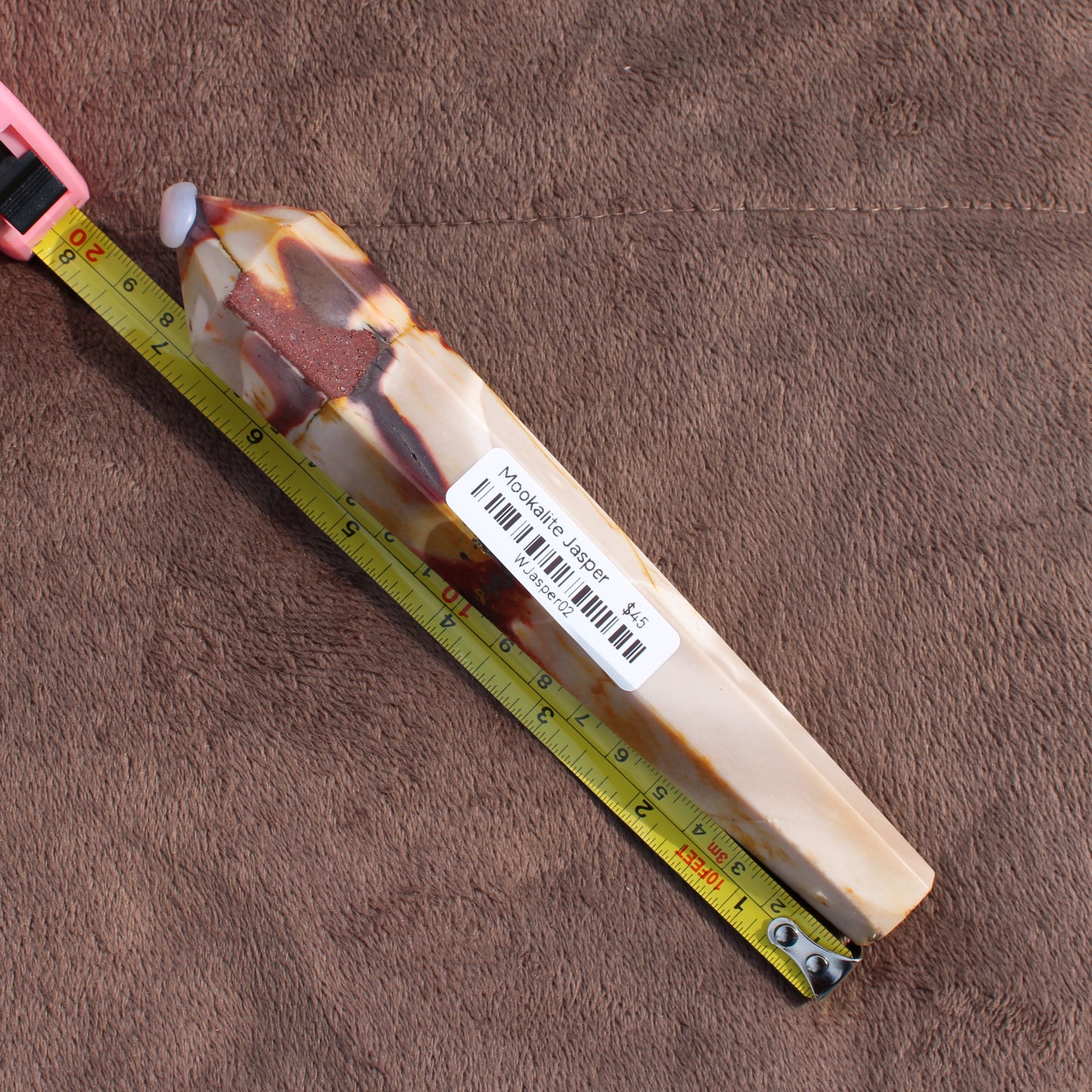 Mookaite Jasper Wand from Different Branches LLC placed next to a measuring tape on a brown surface