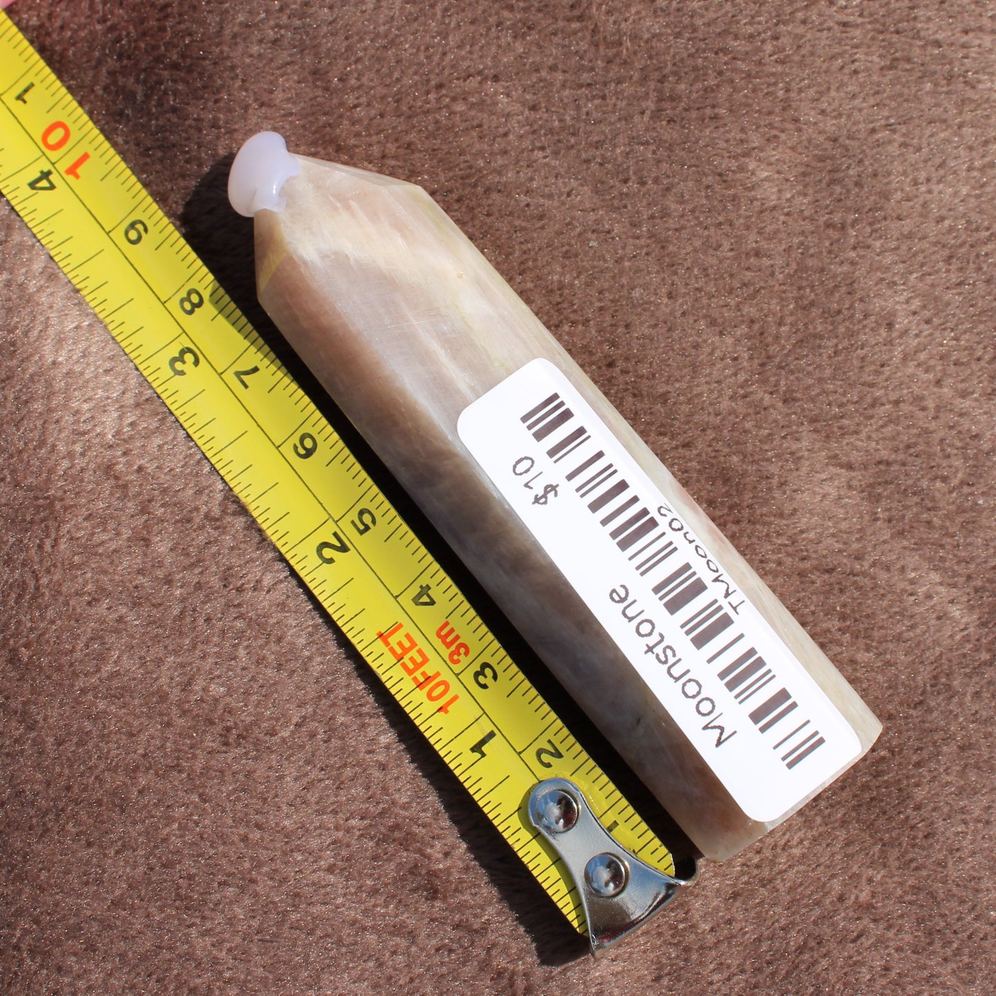 Moonstone Tower crystal with barcode label and yellow measuring tape on brown fabric background