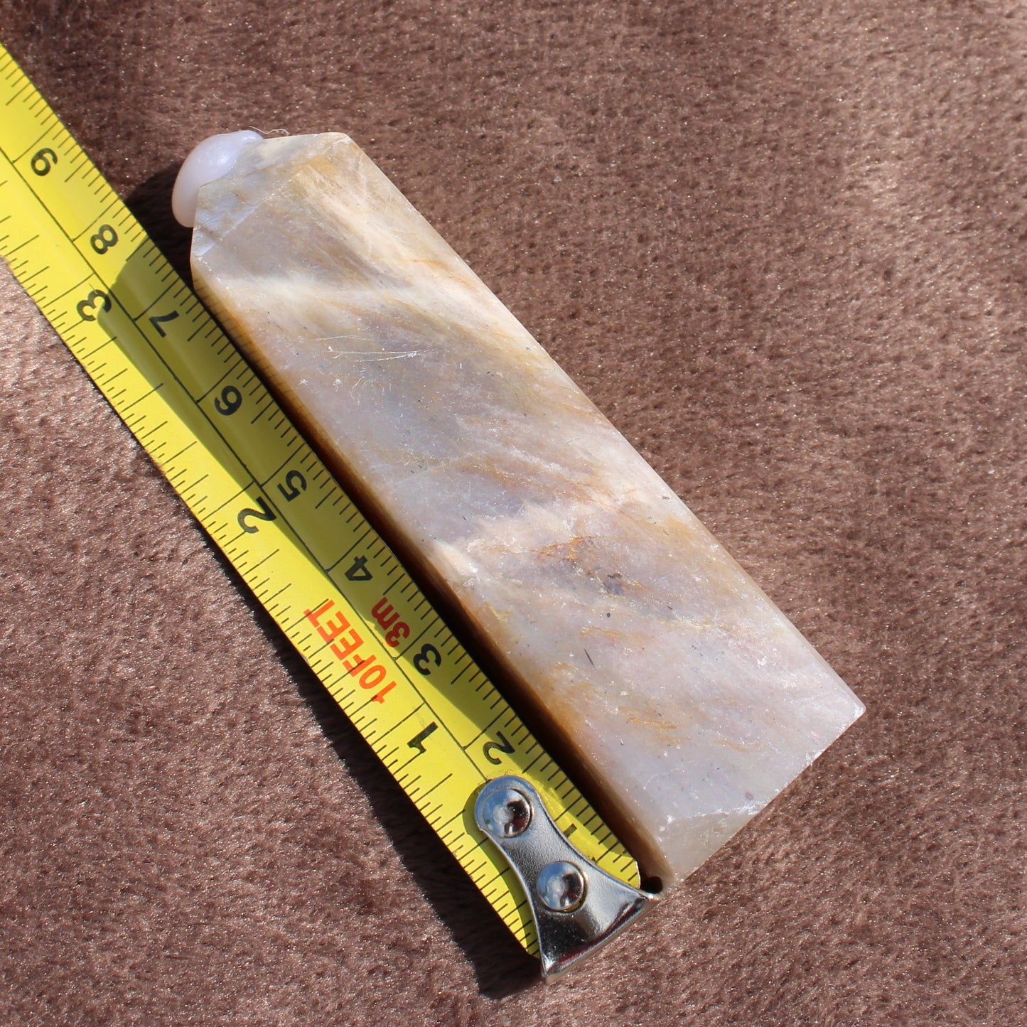 Moonstone Tower crystal measuring about five inches long placed beside a yellow tape measure