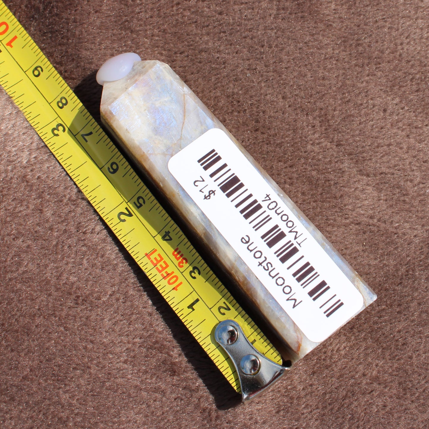 Moonstone Tower crystal from Different Branches LLC next to measuring tape showing size on brown fabric