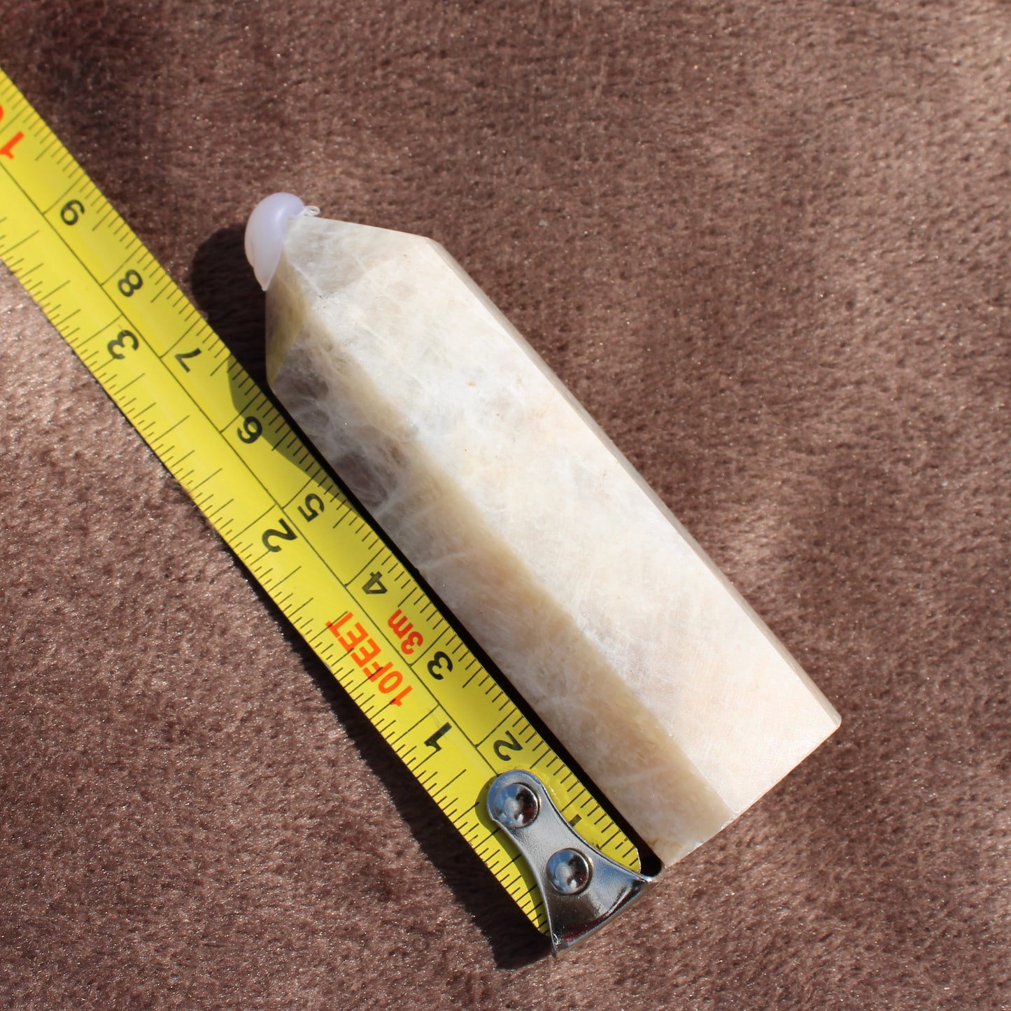 Moonstone Tower crystal from Different Branches LLC next to measuring tape on brown fabric background