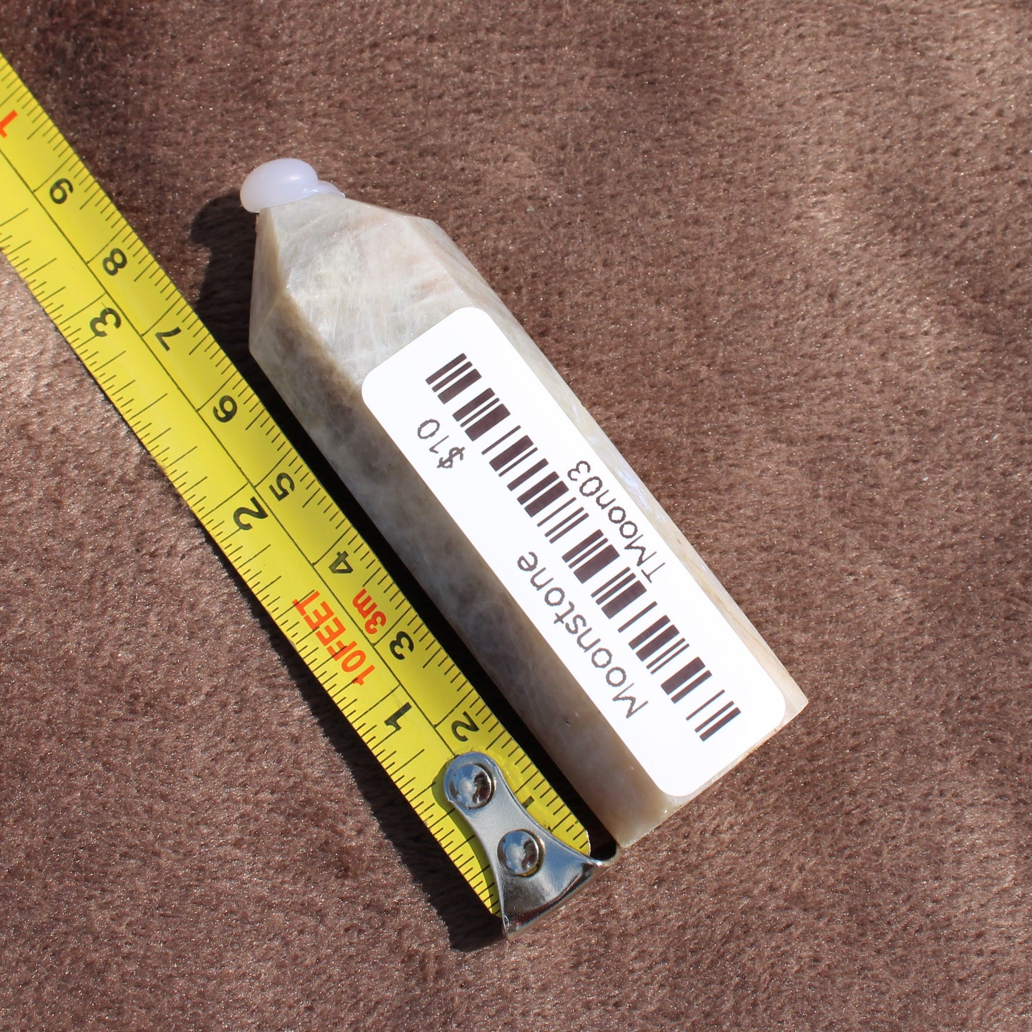 Moonstone Tower crystal from Different Branches LLC placed next to a yellow measuring tape on brown fabric