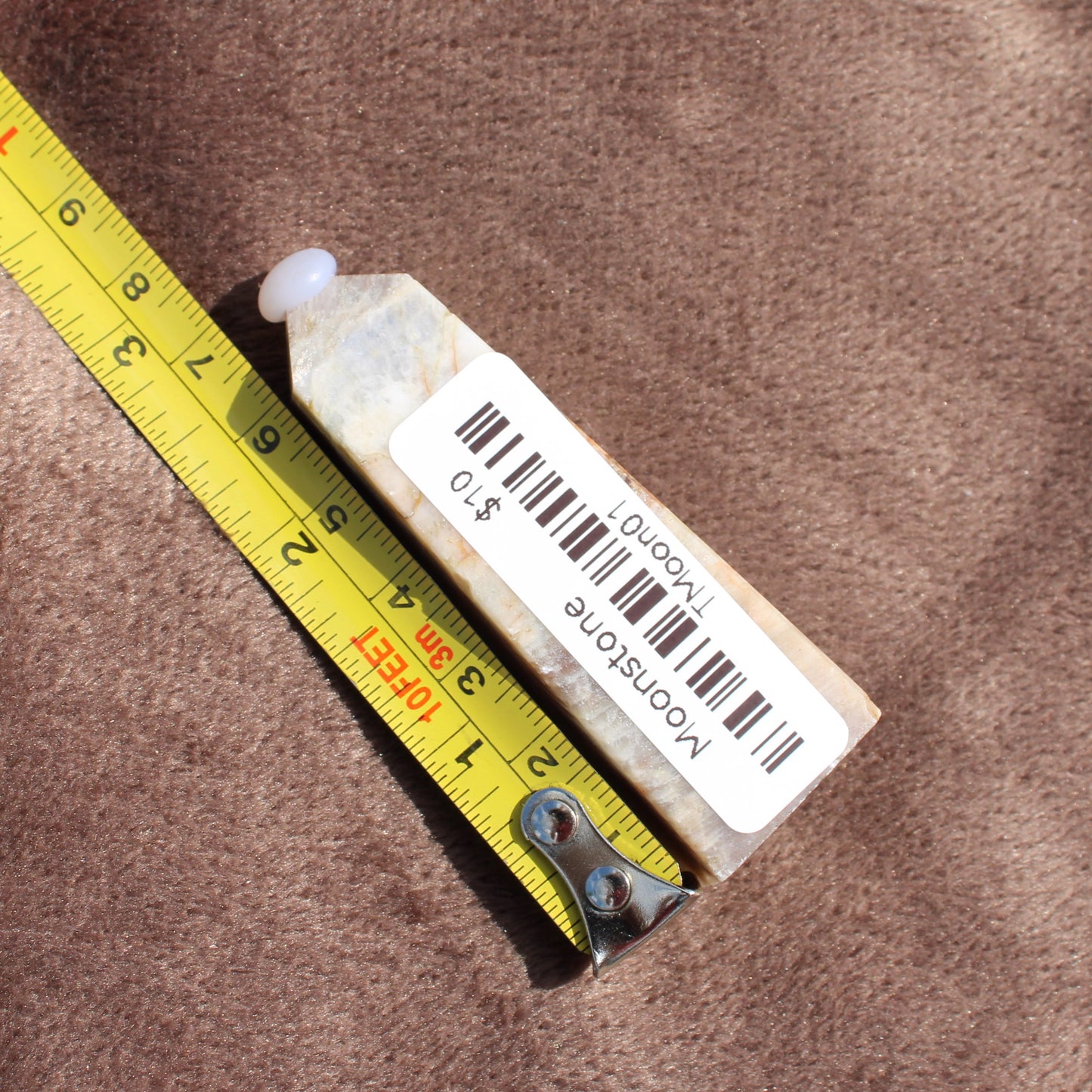 Moonstone Tower crystal from Different Branches LLC placed next to a measuring tape on a brown surface