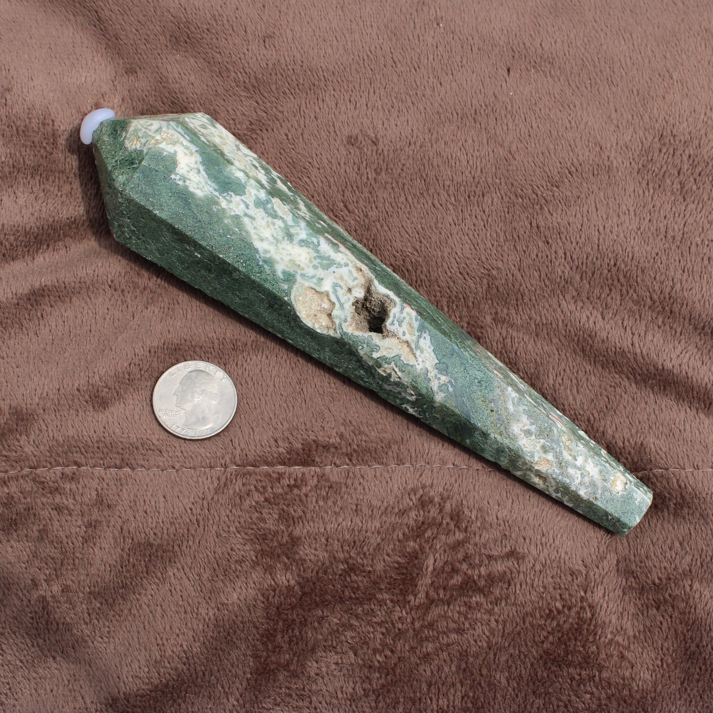 Different Branches LLC Moss Agate Wand crystal with green and white patterns next to a US quarter for size