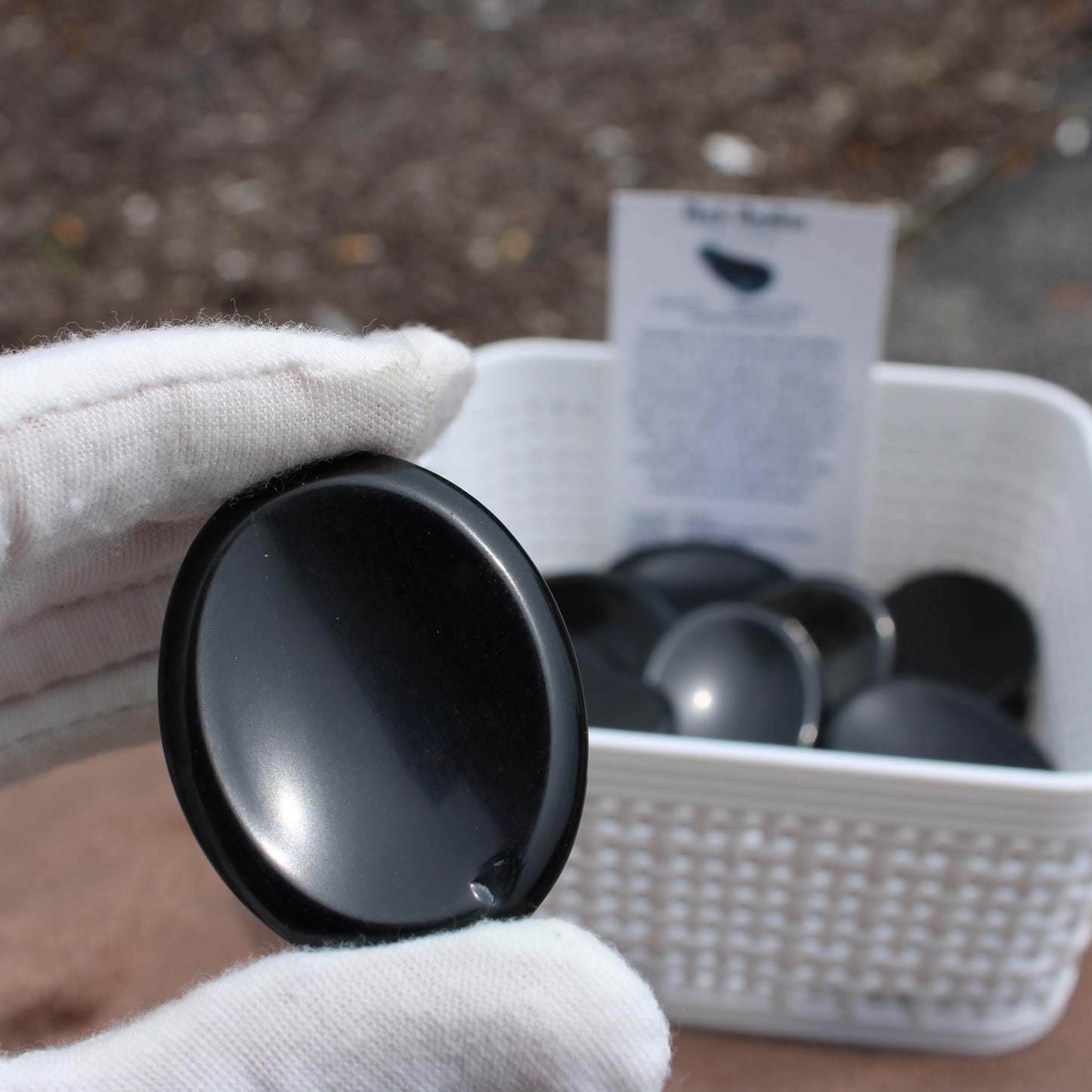 Obsidian Worry Stone held by gloved hand with more stones in white basket by Different Branches LLC