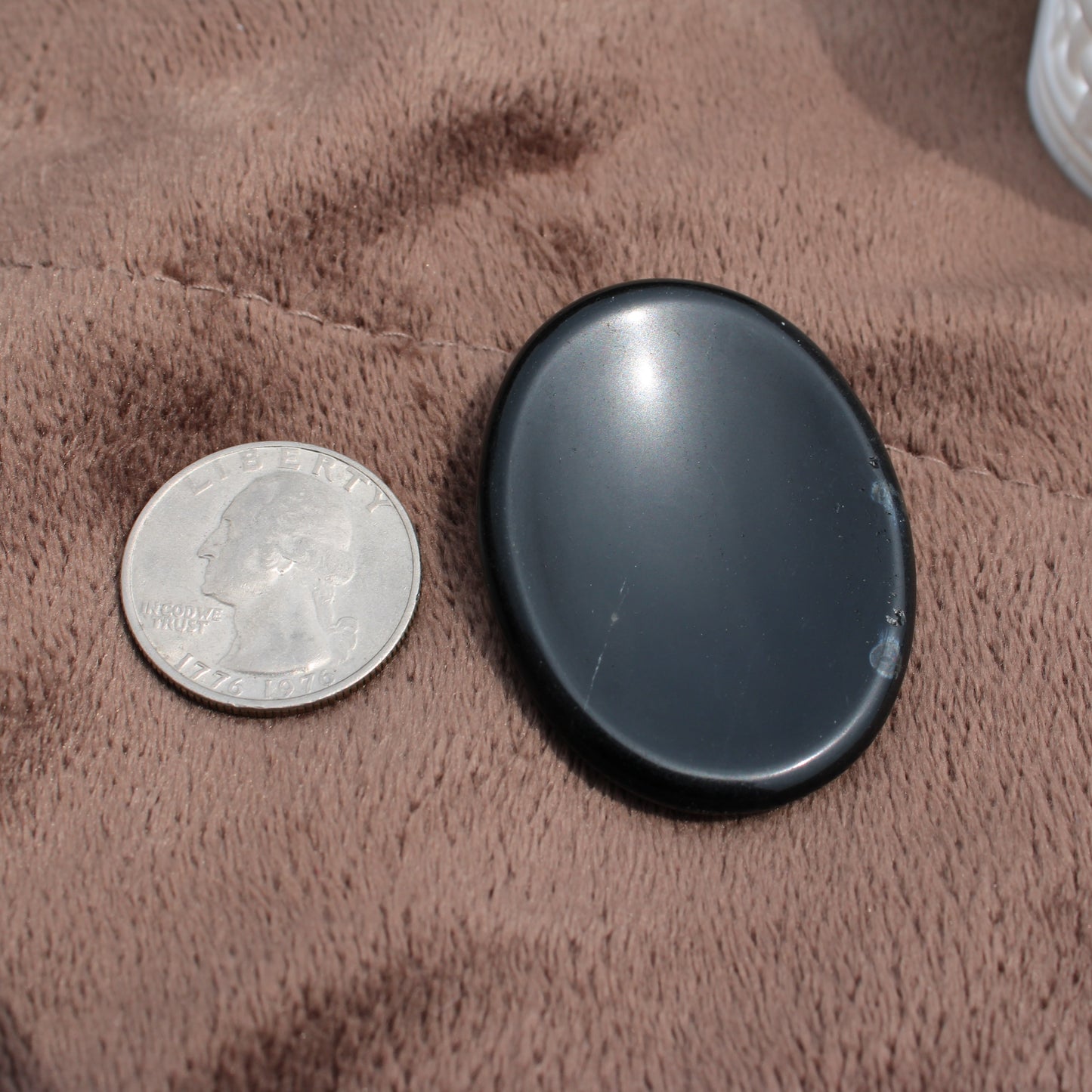 Smooth black Obsidian Worry Stone next to a quarter on brown fabric by Different Branches LLC