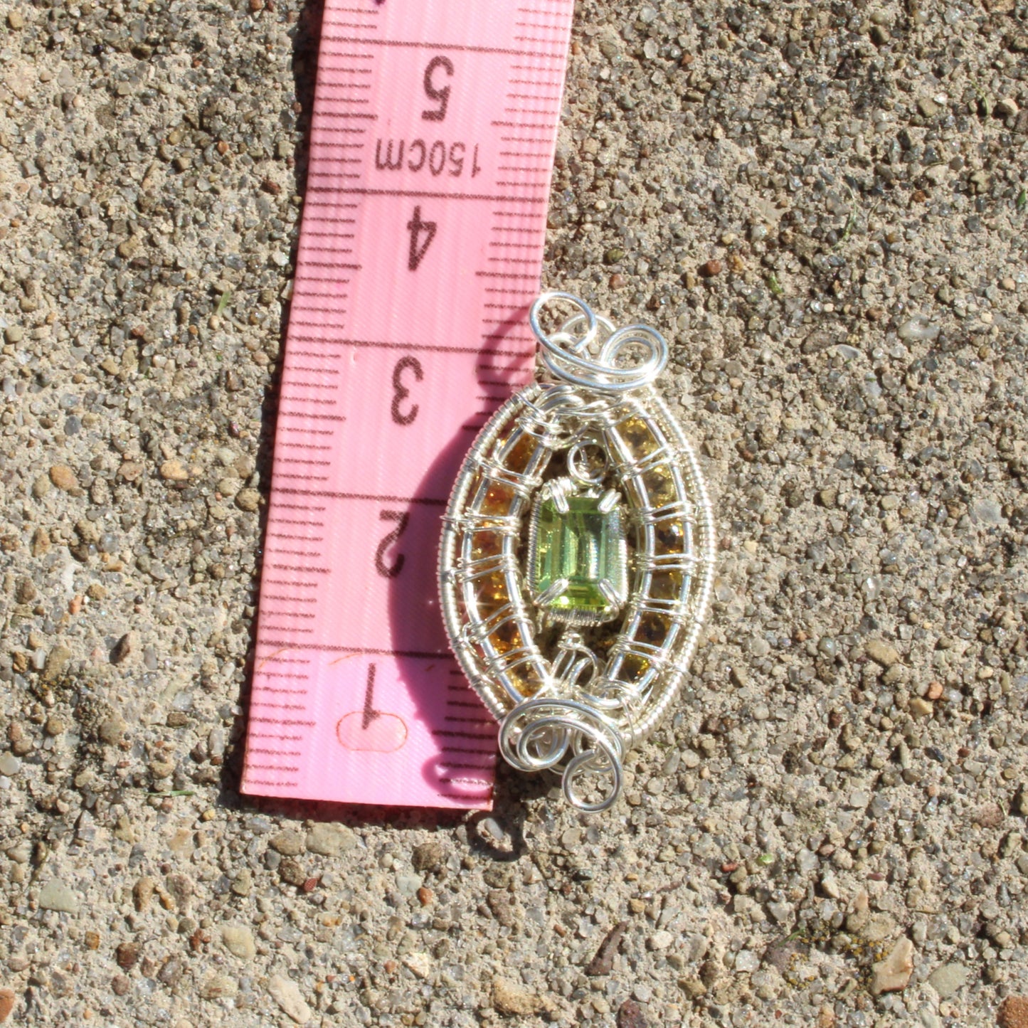 Peridot Sterling Silver yellow tourmaline pendant with intricate wire design on a measuring tape