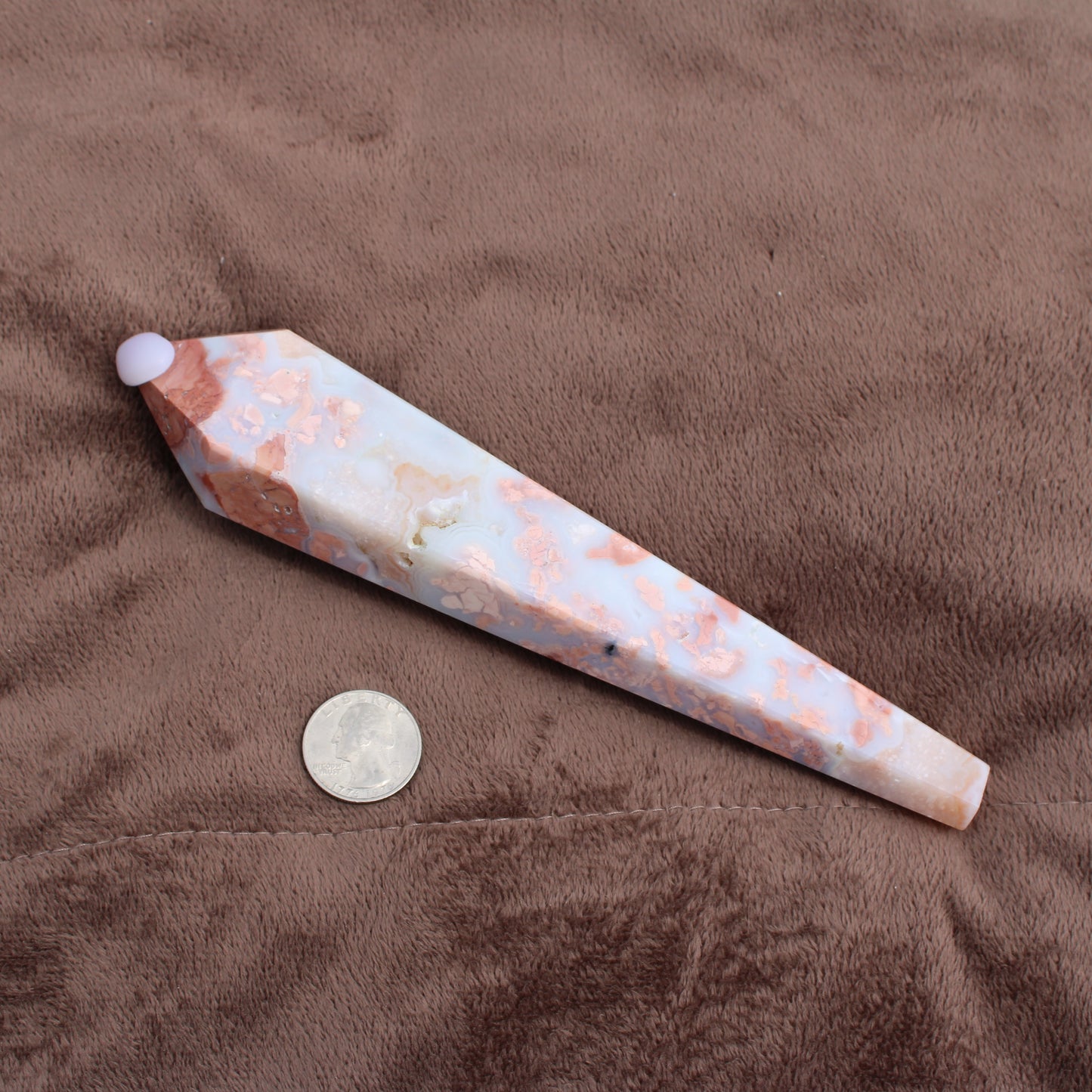 Pink Agate Wand with white and peach tones placed next to a quarter for size reference on brown fabric
