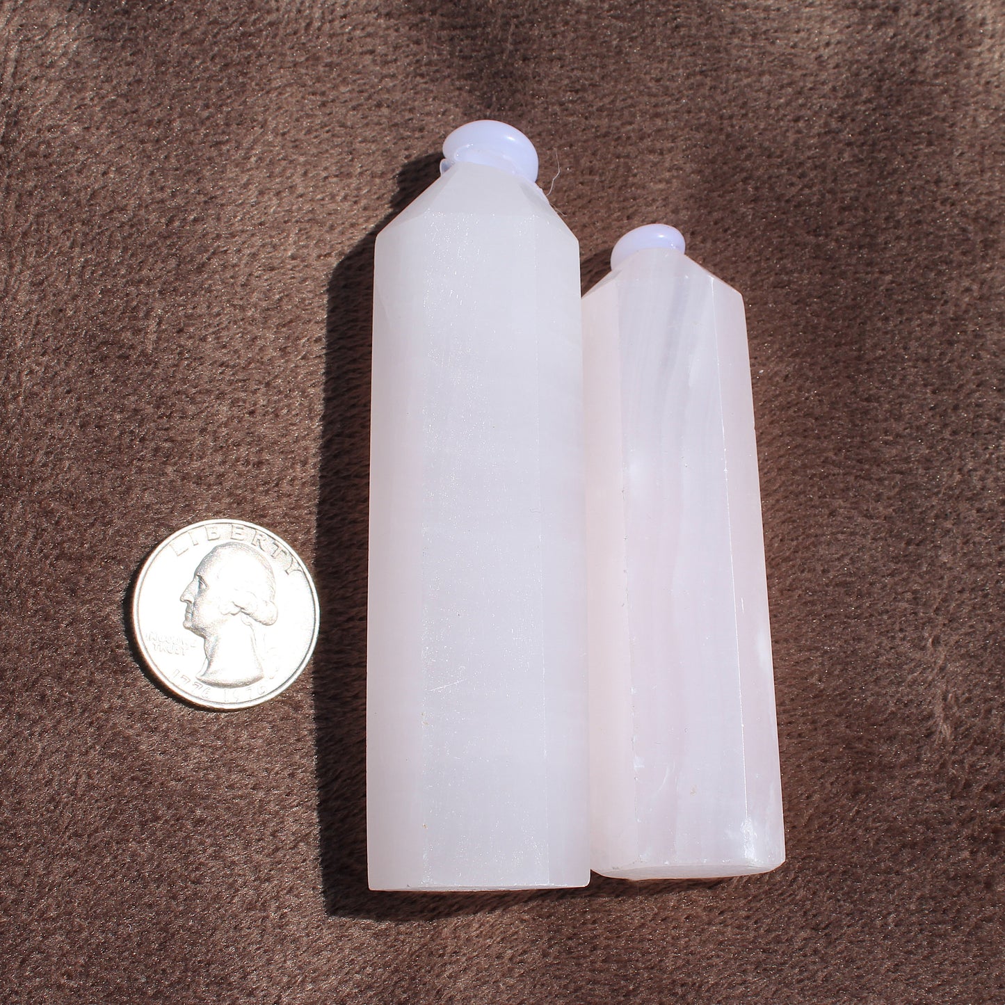 Two polished pink calcite towers beside a US quarter coin for size reference on brown fabric