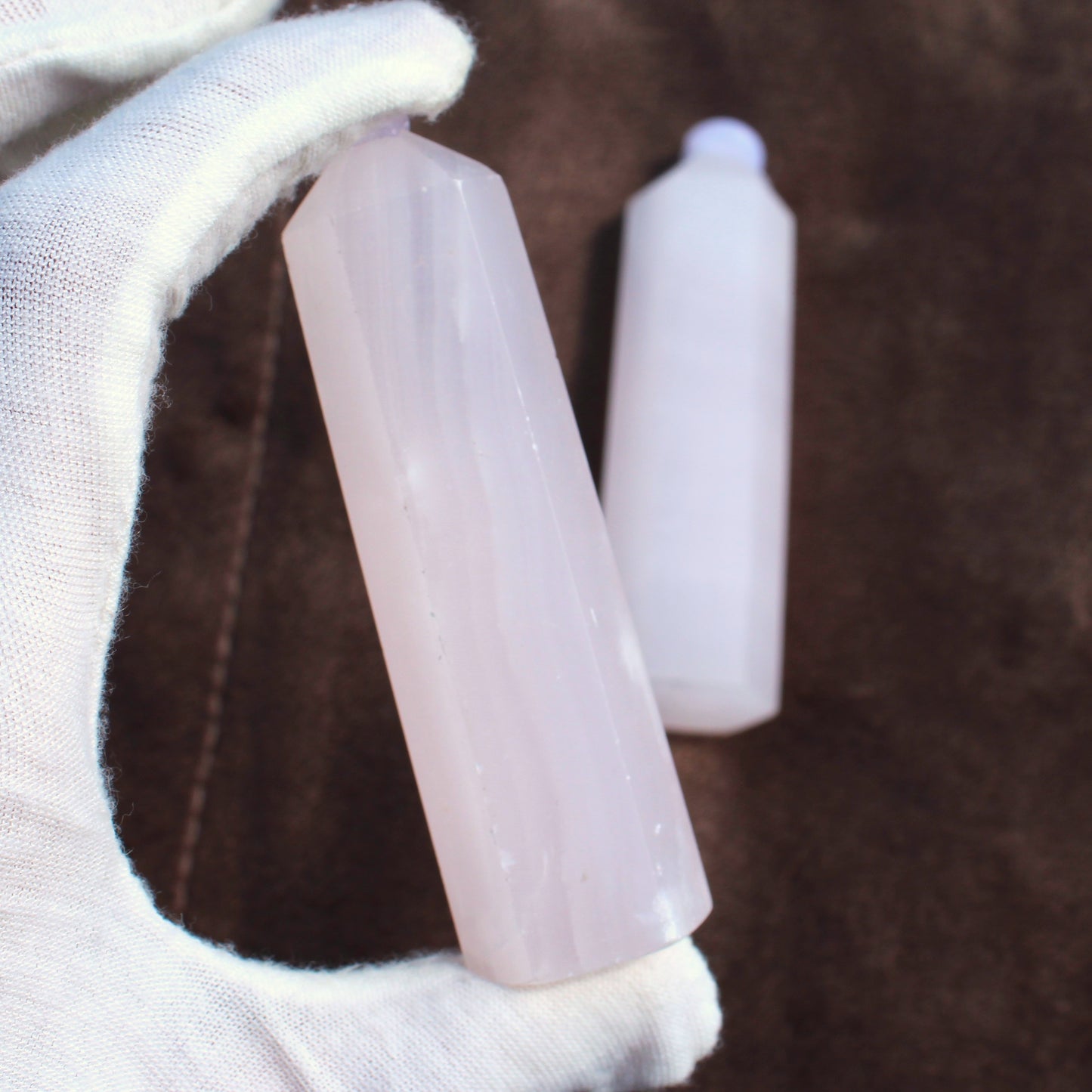 Hand holding a polished Pink Calcite Tower crystal with a brown background