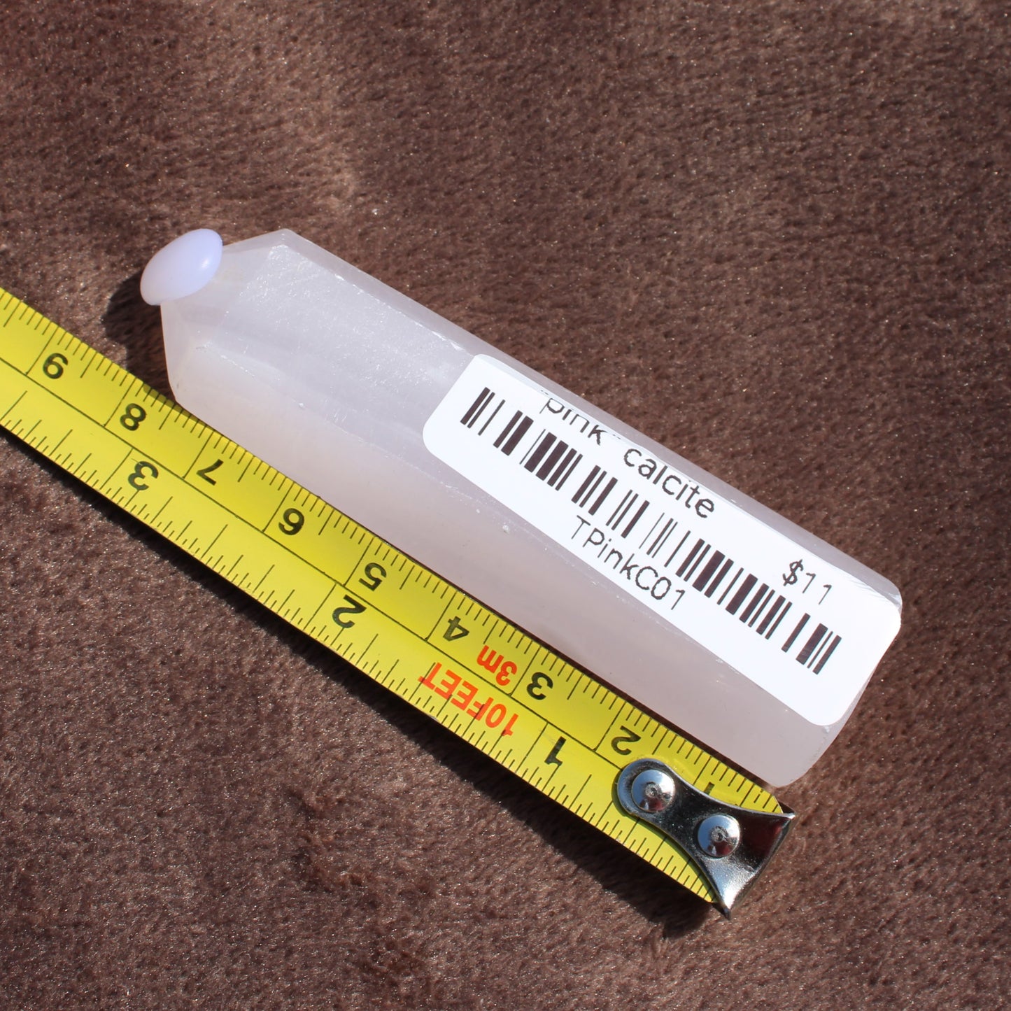 Pink Calcite Tower crystal from Different Branches LLC next to measuring tape showing size on brown background