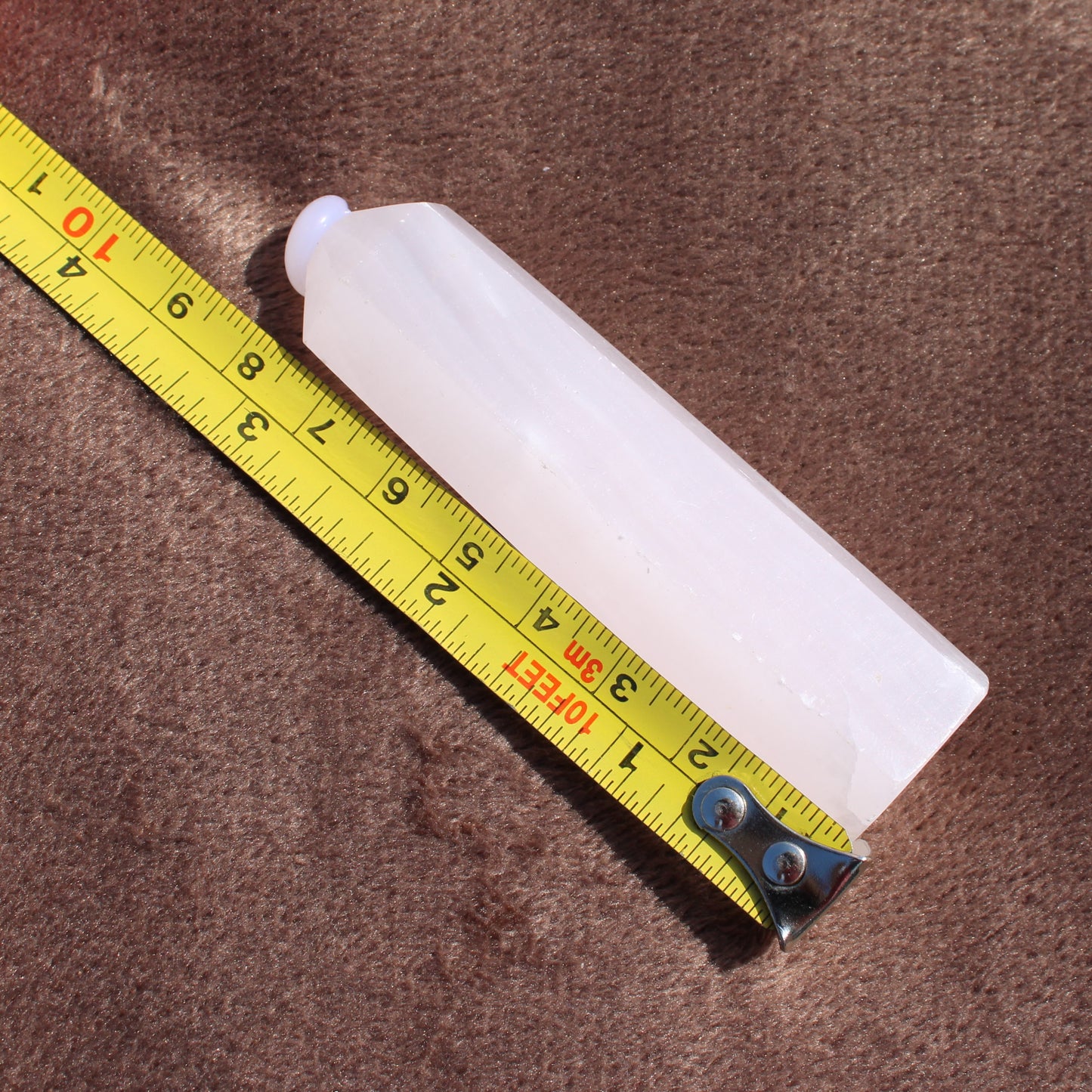 Pink Calcite Tower crystal from Different Branches LLC measured with a yellow tape on brown fabric