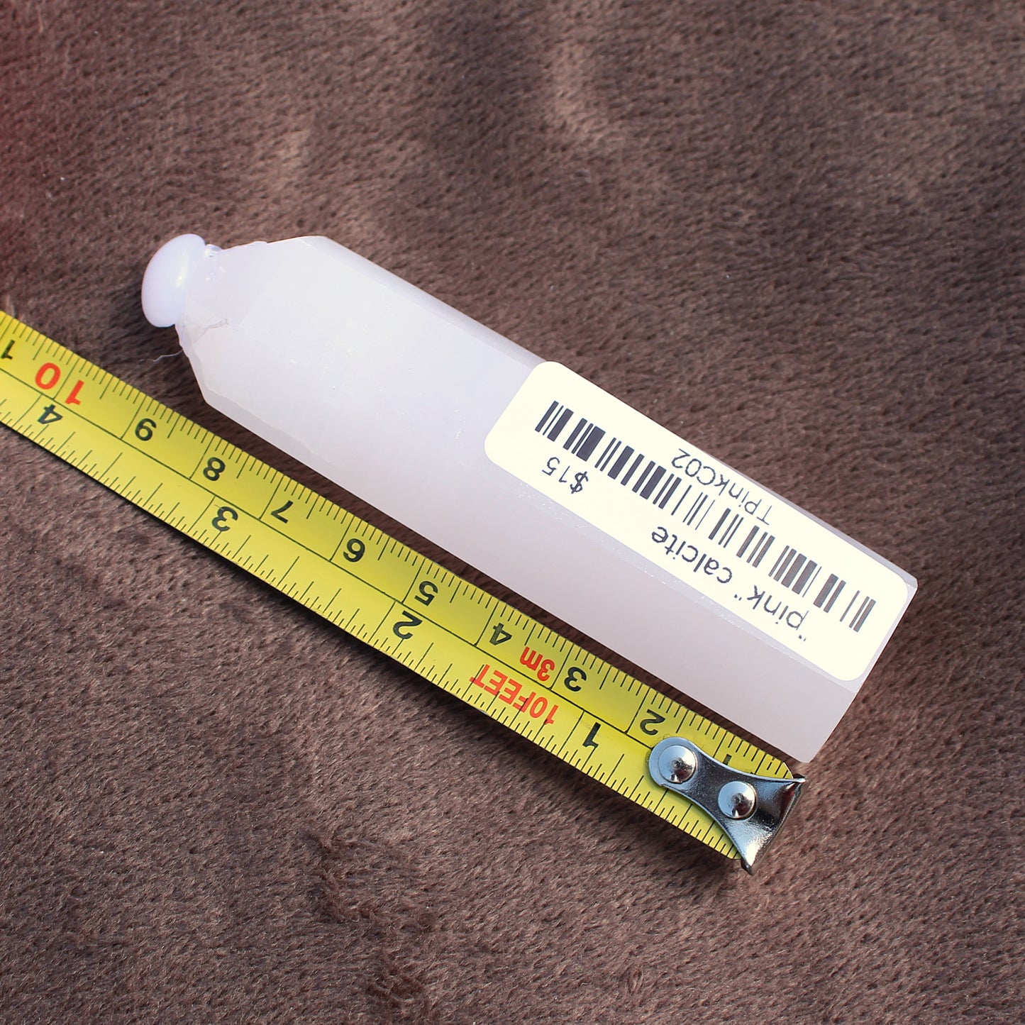Pink Calcite Tower crystal with a price tag placed next to a measuring tape on a brown surface