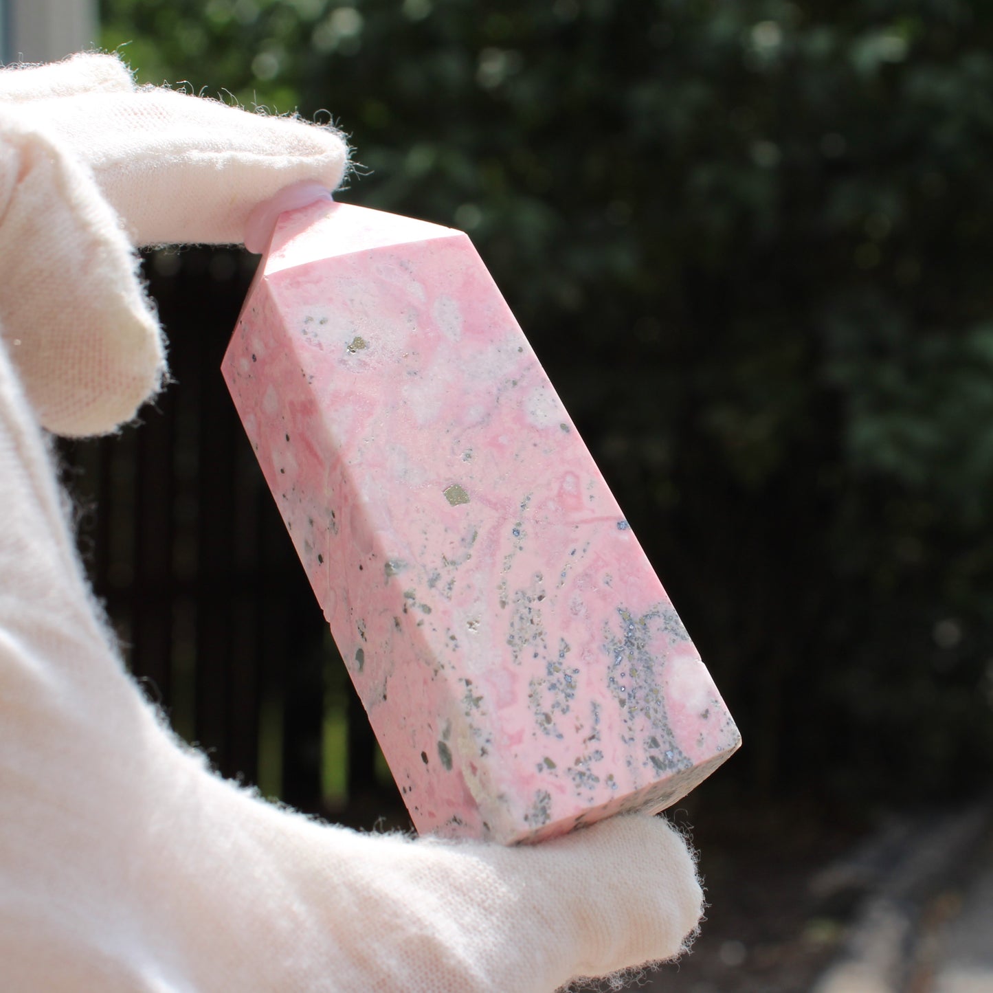 Pink Opal Tower crystal held in gloved hand with natural outdoor background by Different Branches LLC