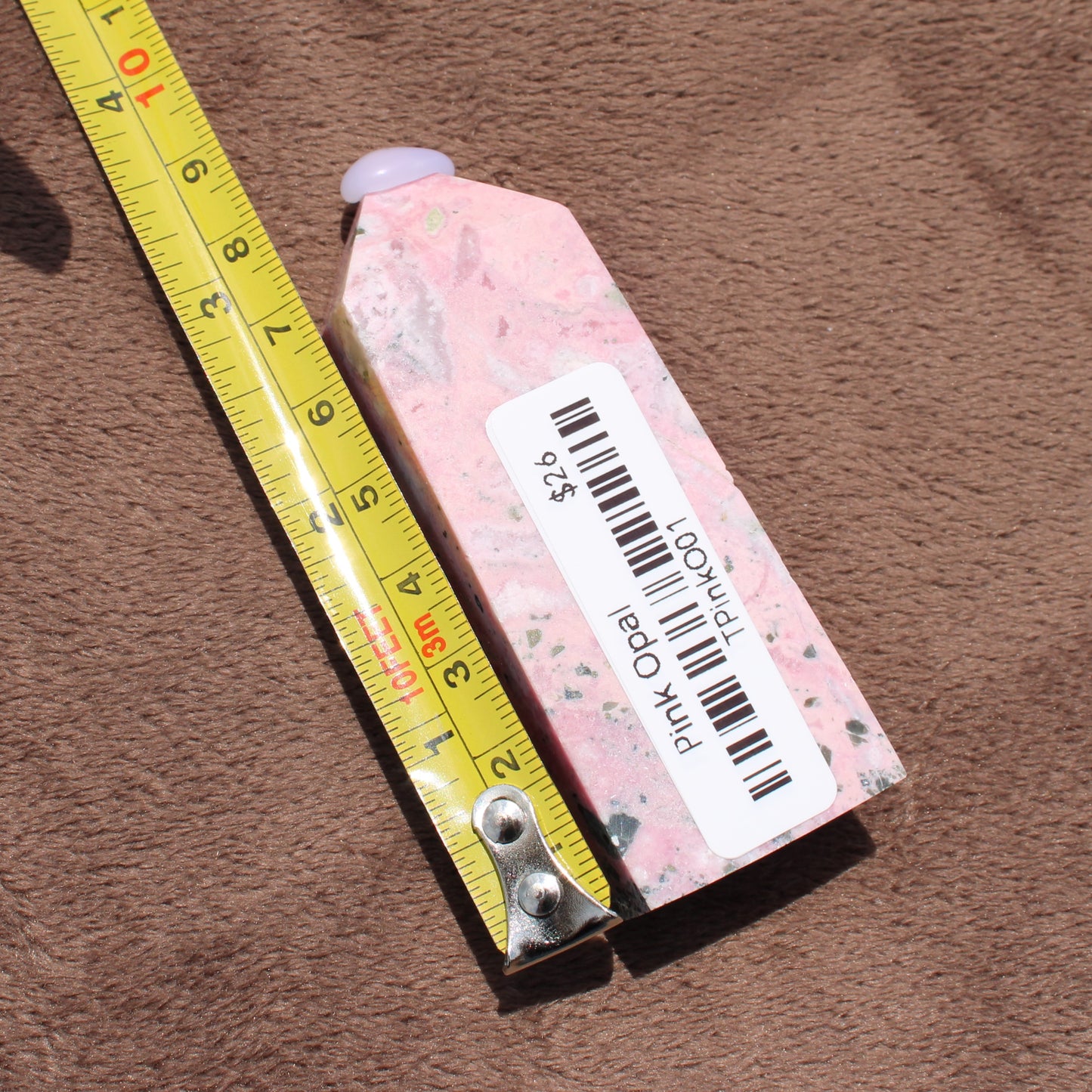 Pink Opal Tower crystal next to a measuring tape showing its size on a brown fabric background
