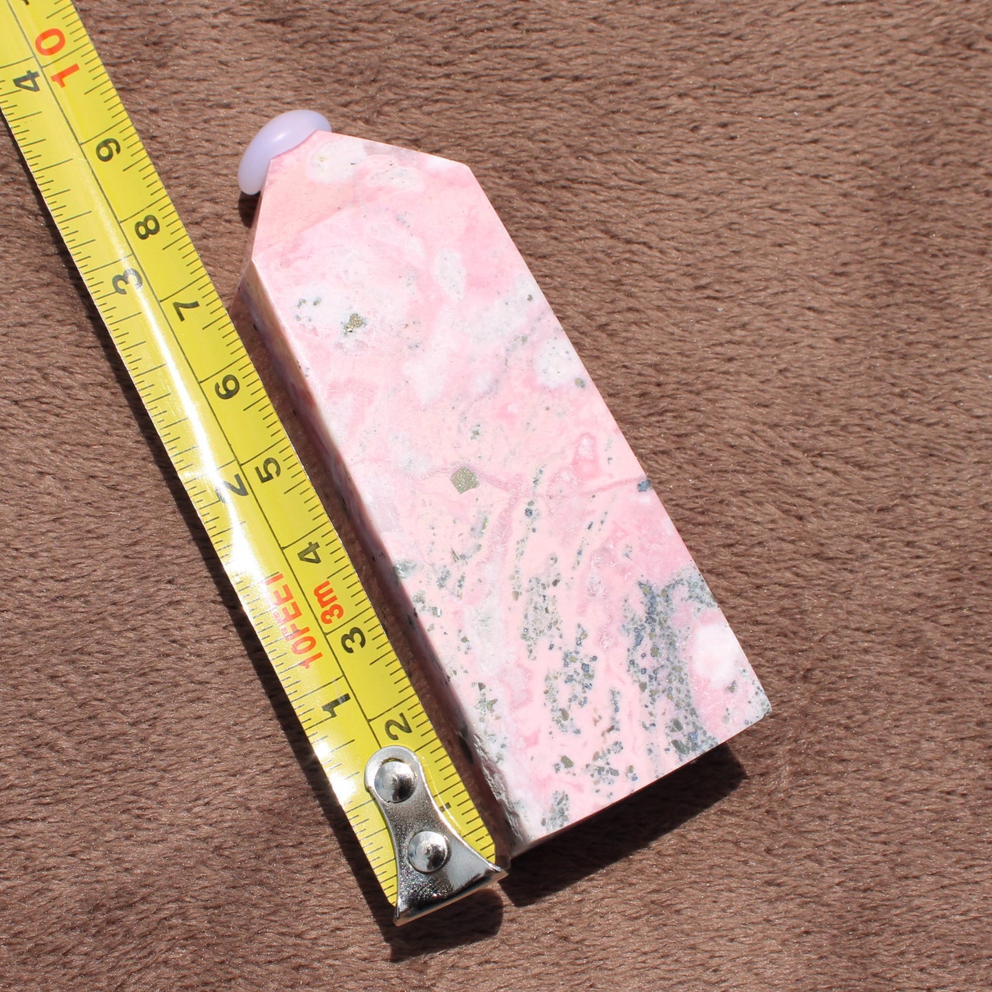 Pink Opal Tower crystal with natural pink and white patterns next to a measuring tape on brown surface