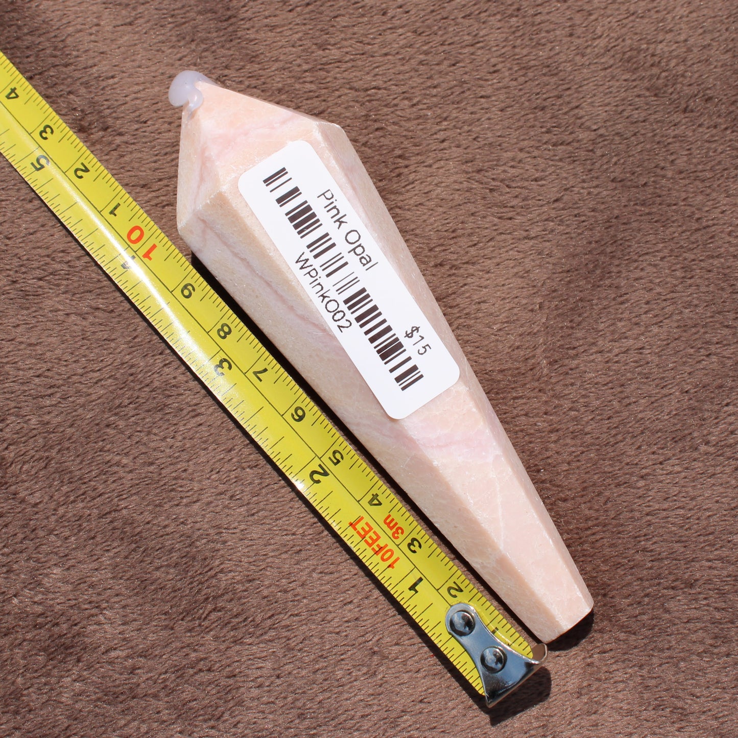Pink Opal Wand crystal from Different Branches LLC next to a measuring tape on brown fabric background