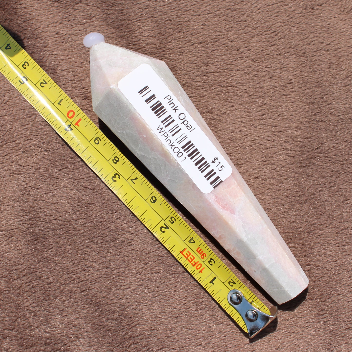 Pink Opal Wand crystal from Different Branches LLC next to measuring tape on brown surface