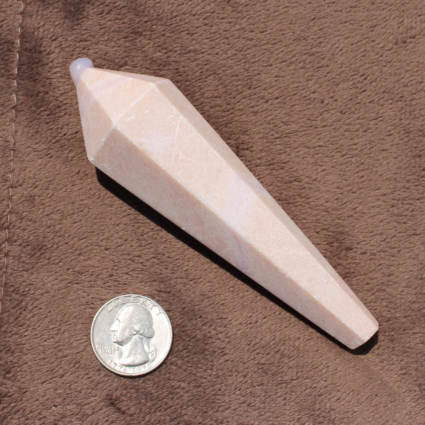 Faceted Pink Opal Wand crystal displayed next to a quarter for size reference on a brown fabric