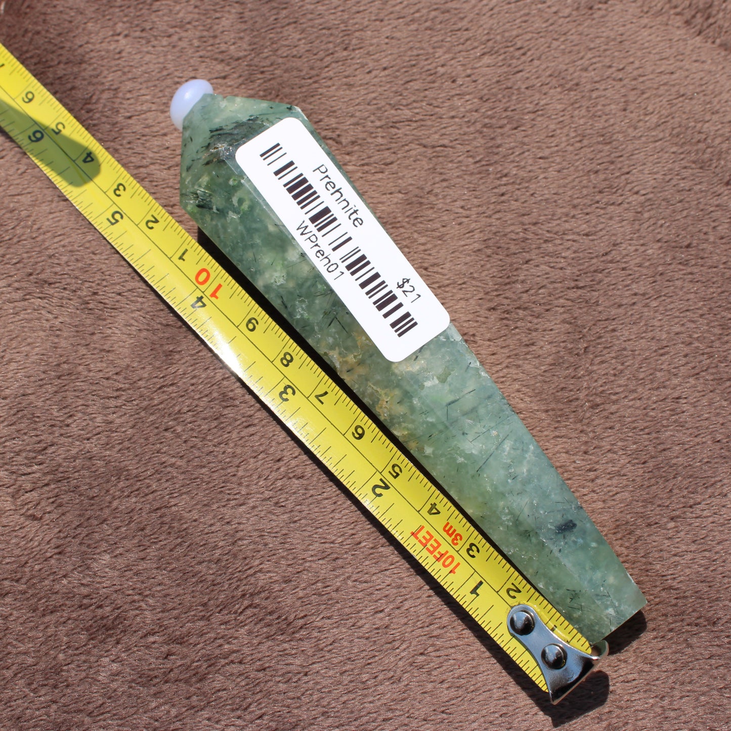 Prehnite Wand crystal measuring about 4 inches placed next to a yellow measuring tape on a brown surface