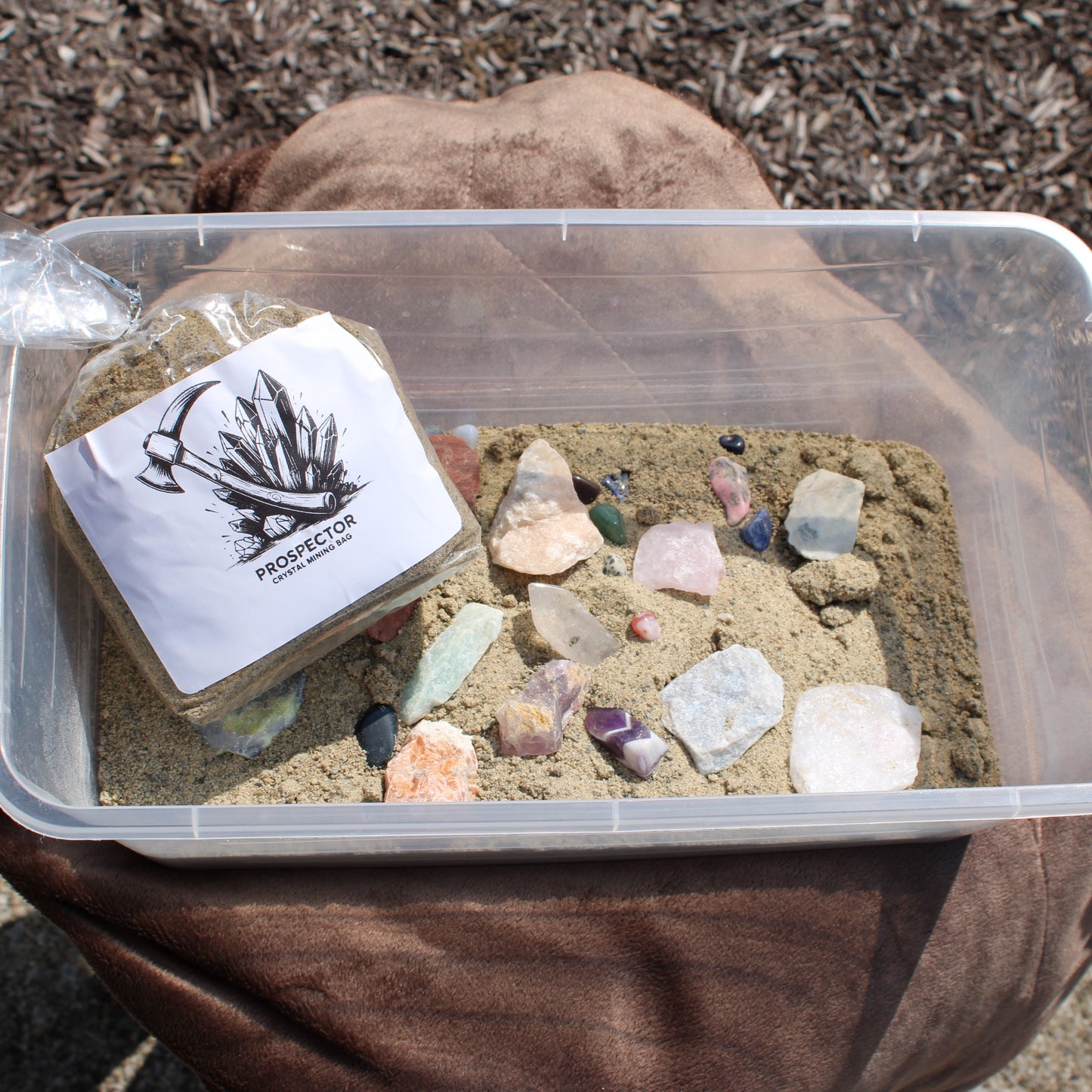 Plastic tub of sand with assorted crystals and rough stones from a large gem mining mystery bag by Different Branches LLC
