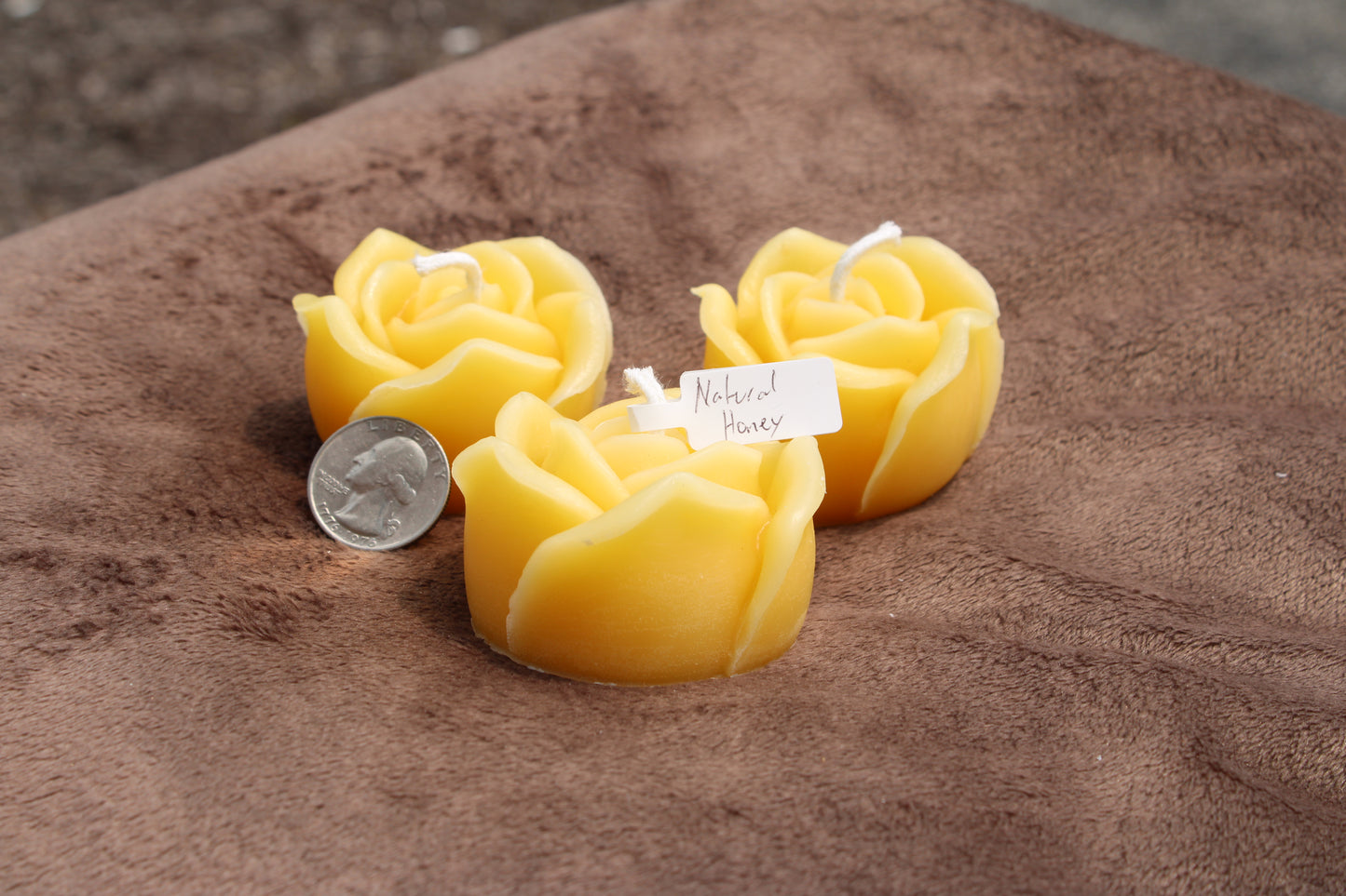 Three pure beeswax rose candles in yellow, shaped like roses, with a quarter for size reference