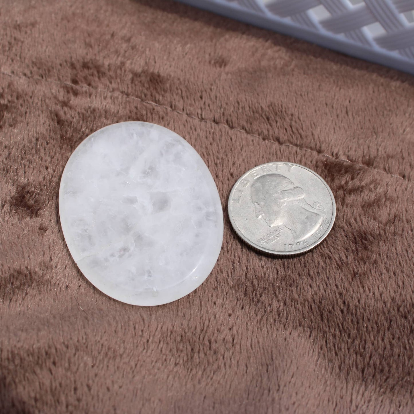 Clear Quartz Worry Stone next to a quarter for size comparison on a brown textured surface