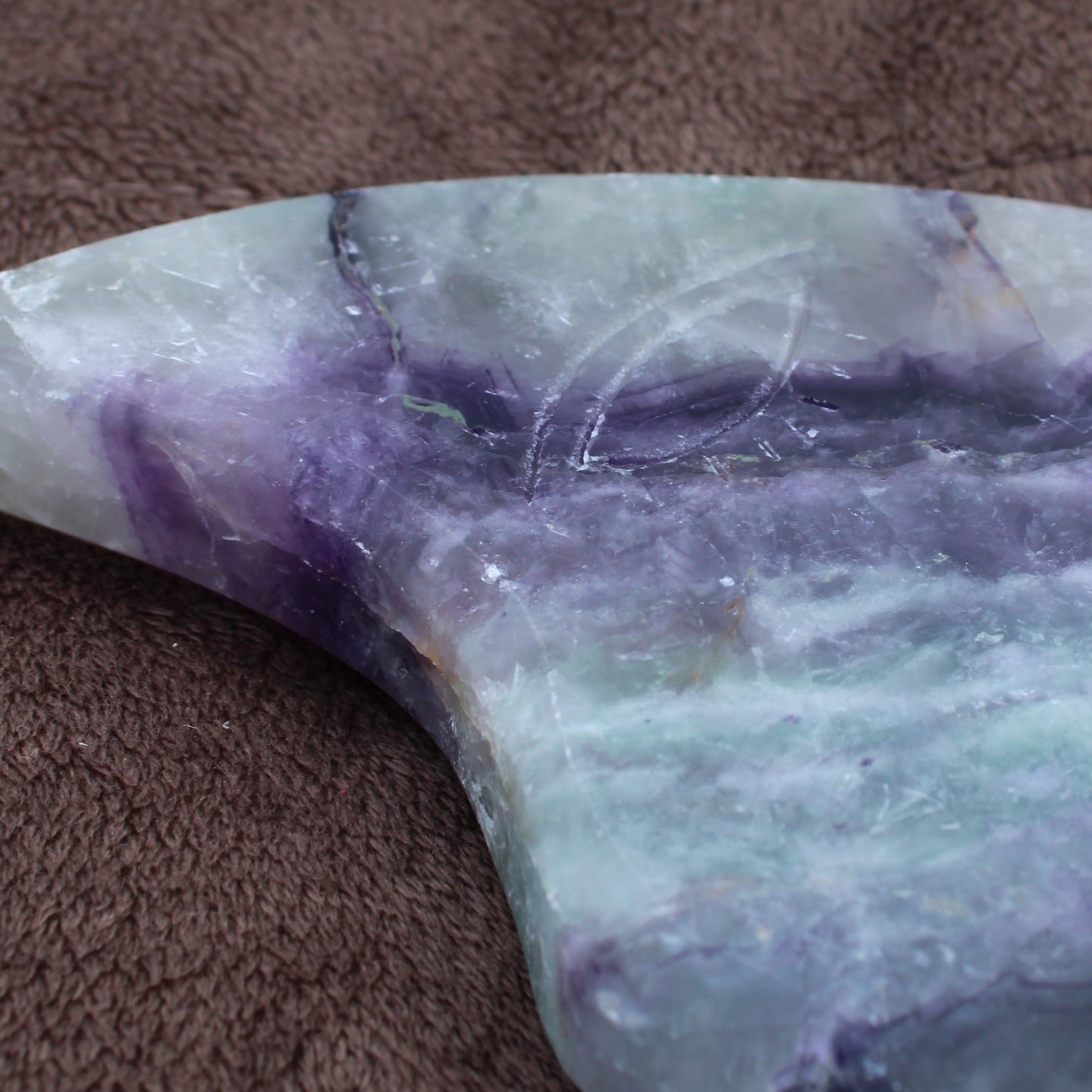 Close-up of Rainbow Fluorite Crescent Moon Statement Crystal with purple and green hues on brown fabric