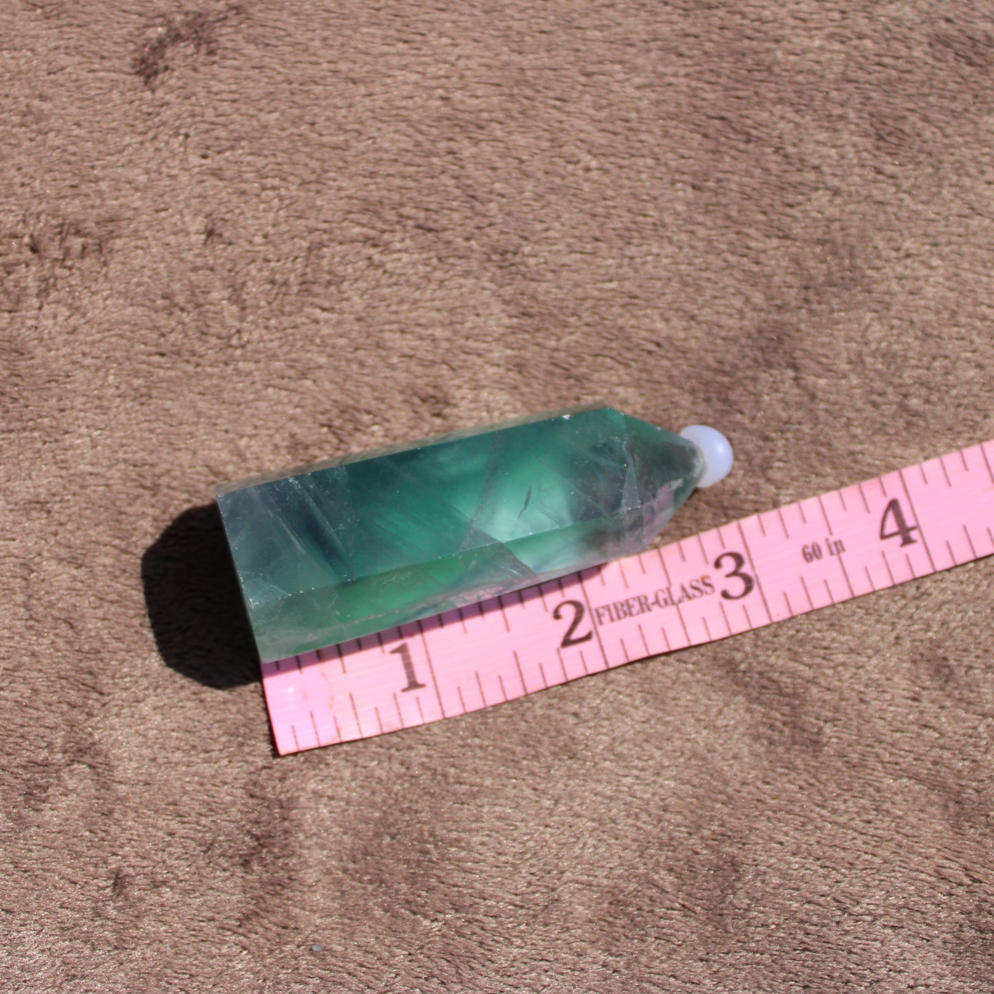 Rainbow Fluorite tower polished crystal showcasing vibrant green and purple hues with a ruler for size reference