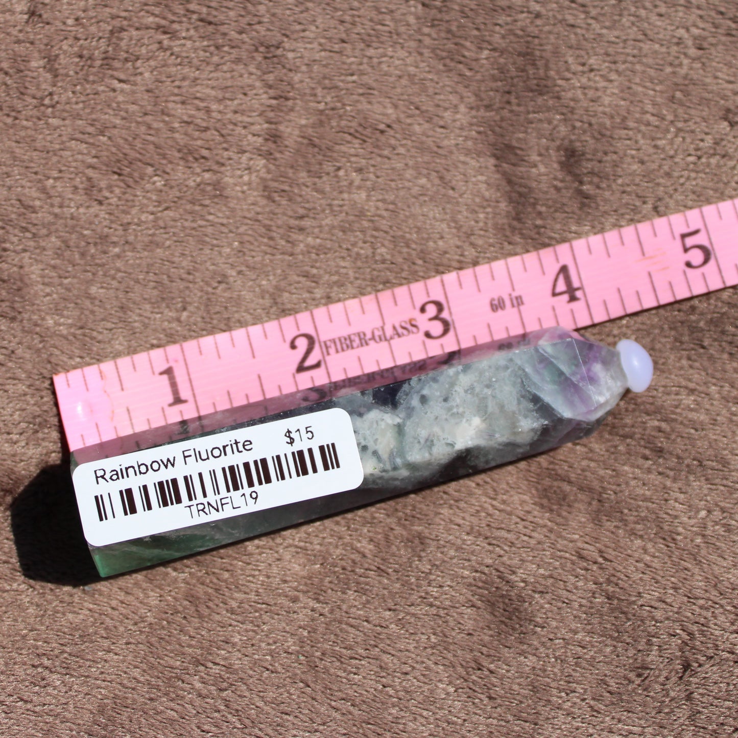 Rainbow Fluorite tower with vibrant colors and unique natural patterns displayed on a sandy background
