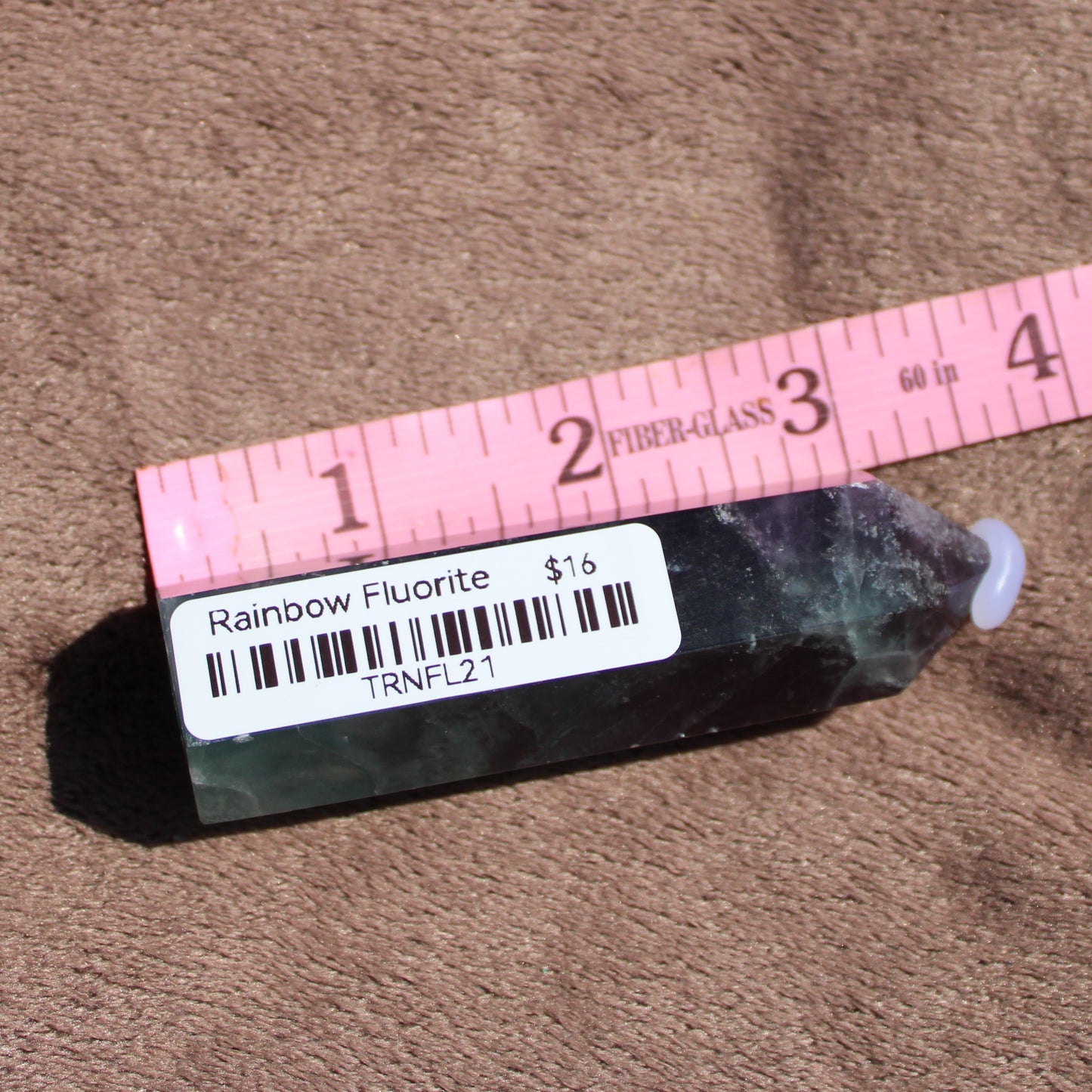 Rainbow Fluorite tower displayed on a textured surface with a ruler for size reference