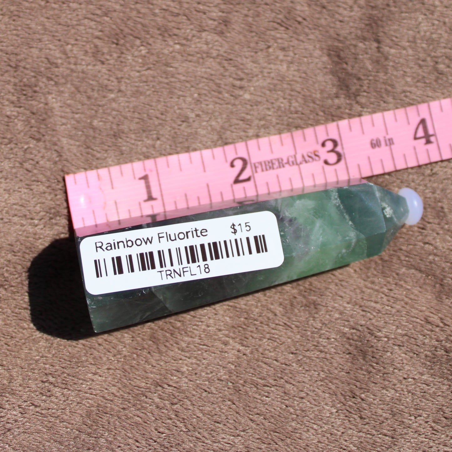 Rainbow Fluorite tower displayed with a ruler, showcasing its vibrant colors and unique shape
