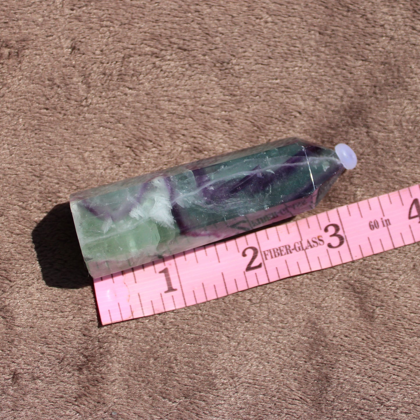 Rainbow Fluorite tower with smooth surface and vibrant green and purple colors on a soft background