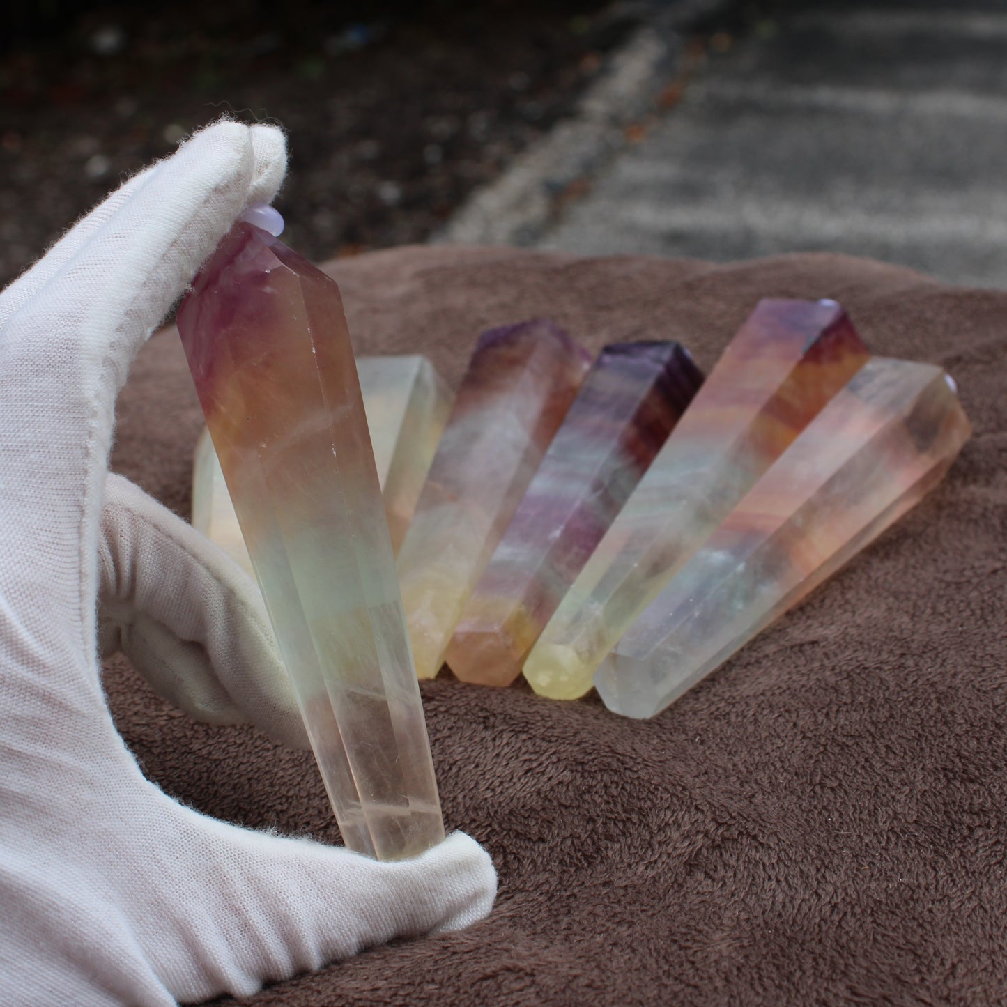 Hand holding a polished Rainbow Fluorite Wand with multiple colorful fluorite wands on brown cloth
