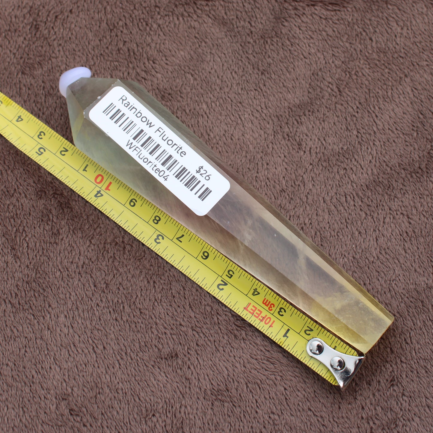 Rainbow Fluorite Wand crystal with label and yellow measuring tape on brown fabric background