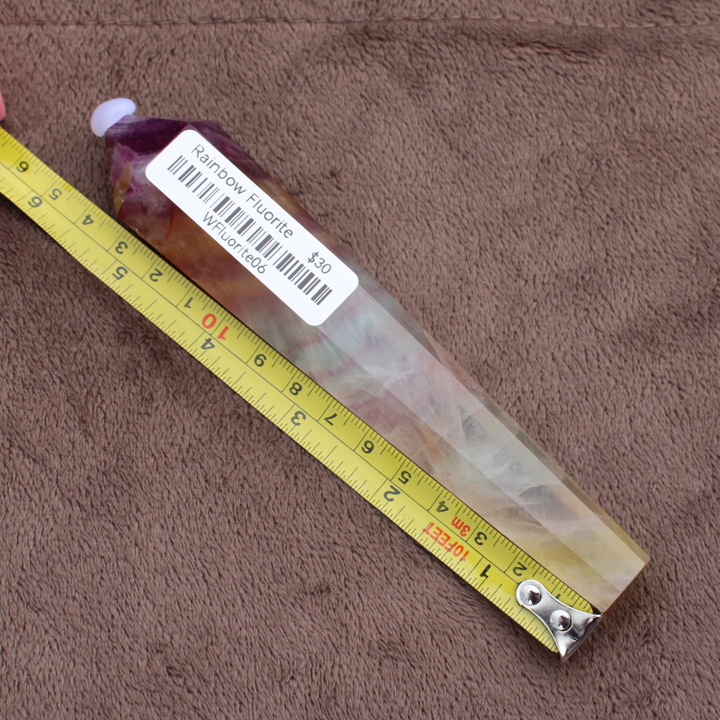 Rainbow Fluorite Wand crystal from Different Branches LLC next to measuring tape on brown fabric