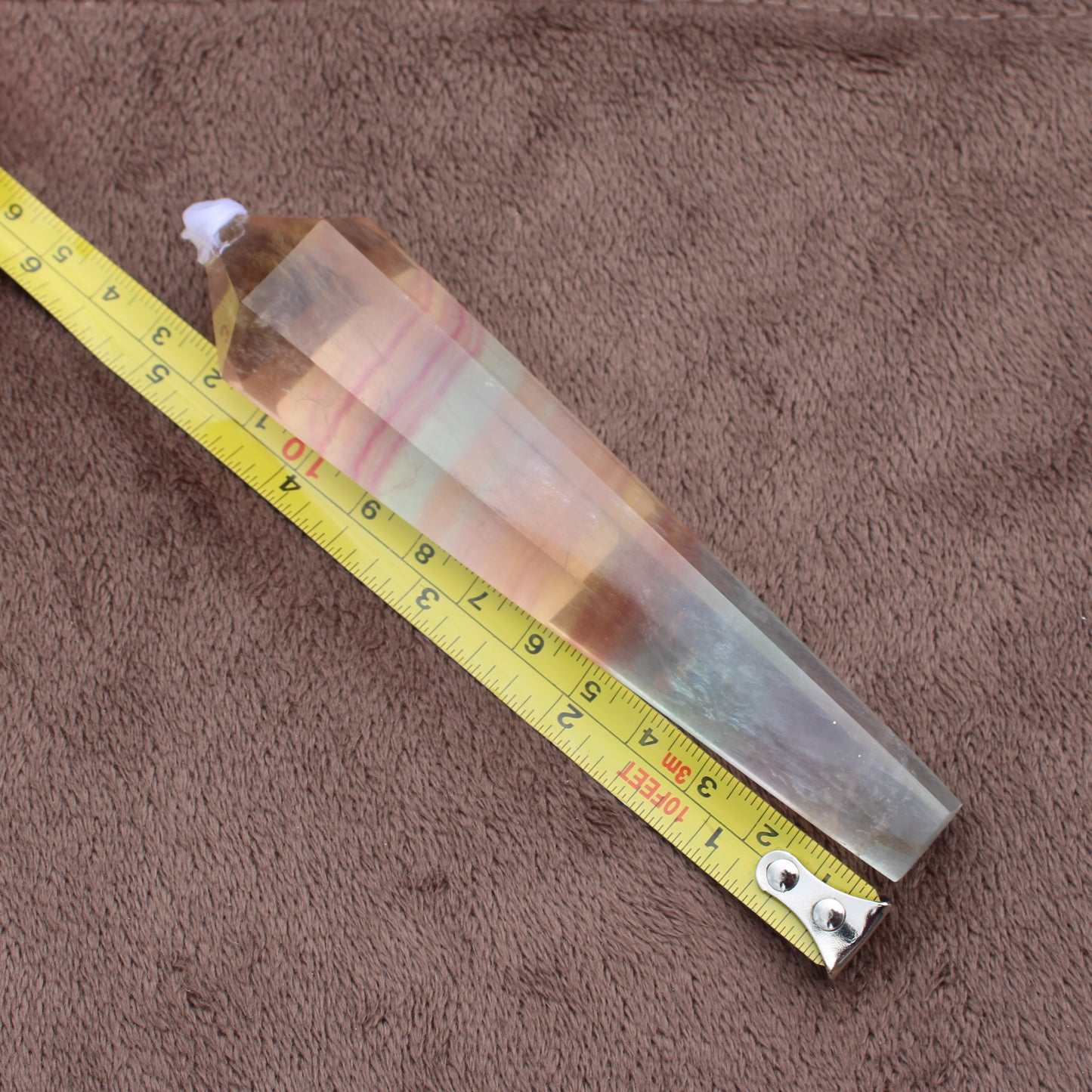 Rainbow Fluorite Wand crystal resting next to a measuring tape on a brown surface