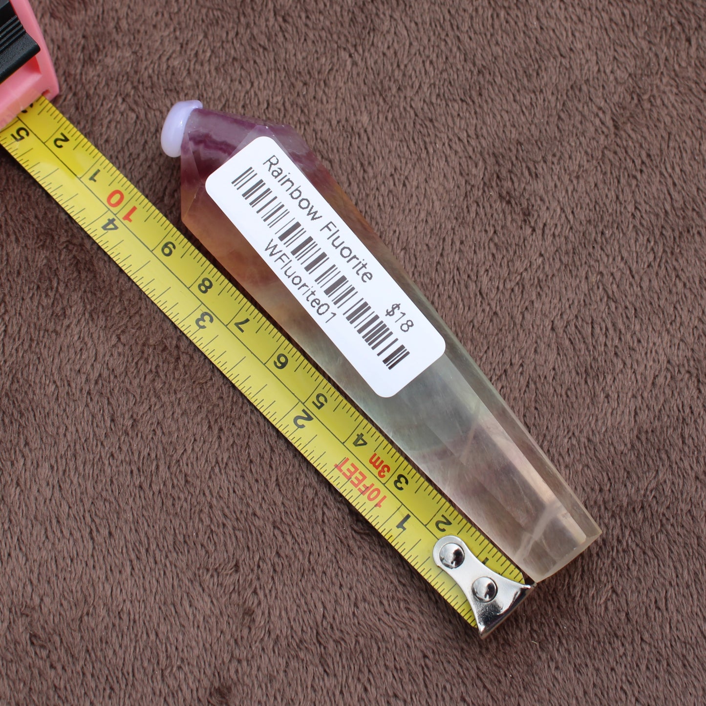 Rainbow Fluorite Wand crystal placed next to a measuring tape on a brown fabric background