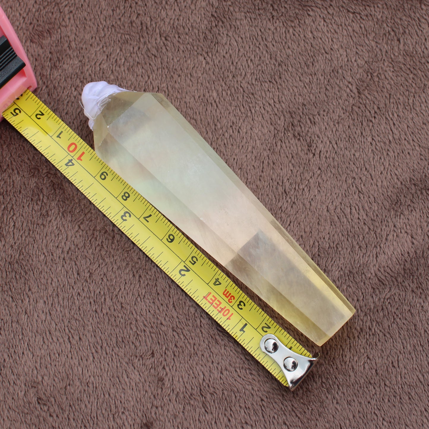 Rainbow Fluorite Wand crystal placed next to yellow measuring tape on brown surface