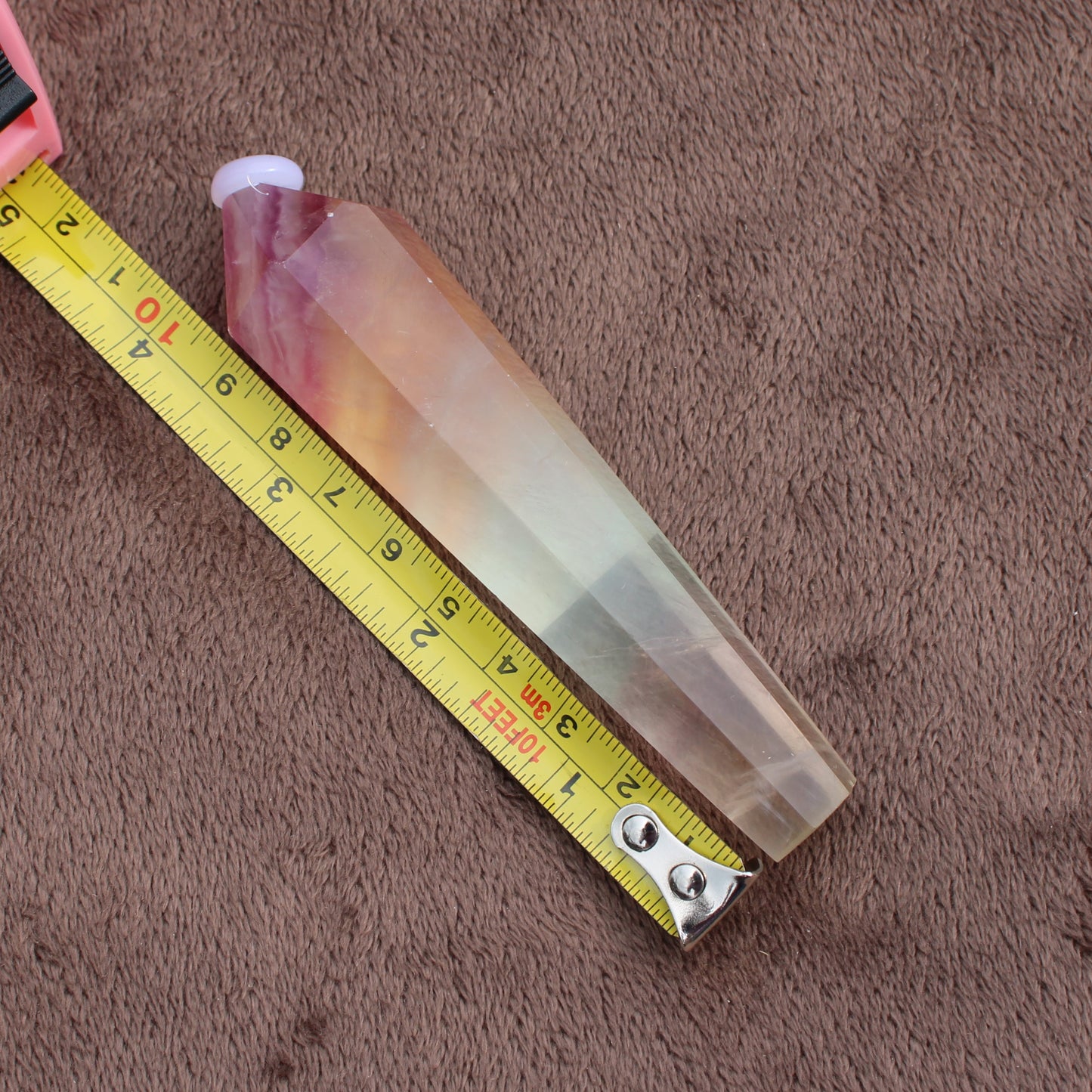 Rainbow Fluorite Wand crystal measuring about six inches placed next to a yellow tape measure on brown fabric