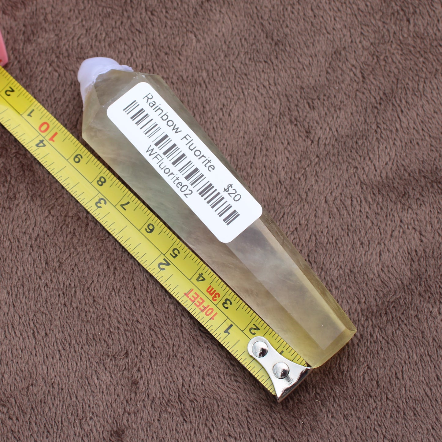 Rainbow Fluorite Wand crystal from Different Branches LLC next to a measuring tape on brown fabric