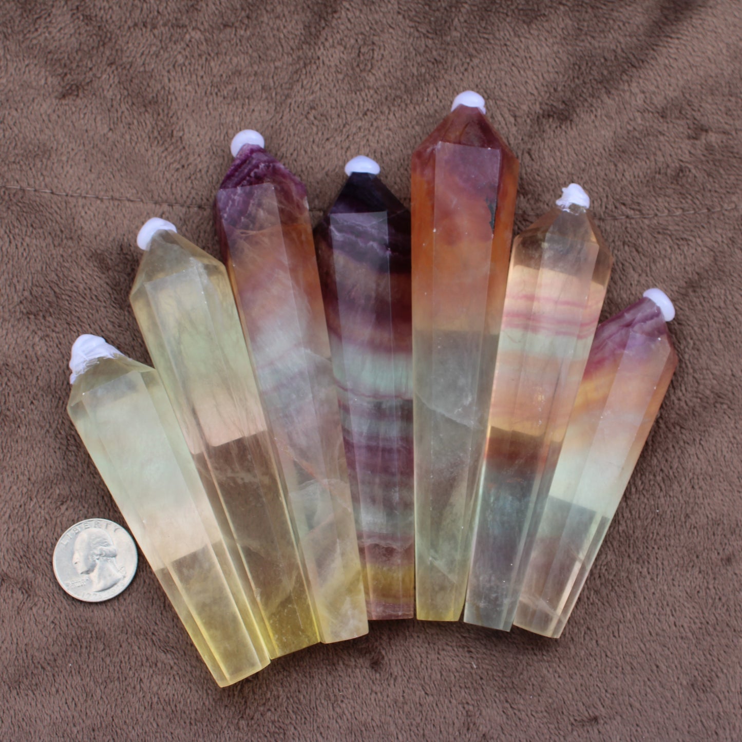 Rainbow Fluorite Wand crystal points in various colors arranged with a quarter for size comparison