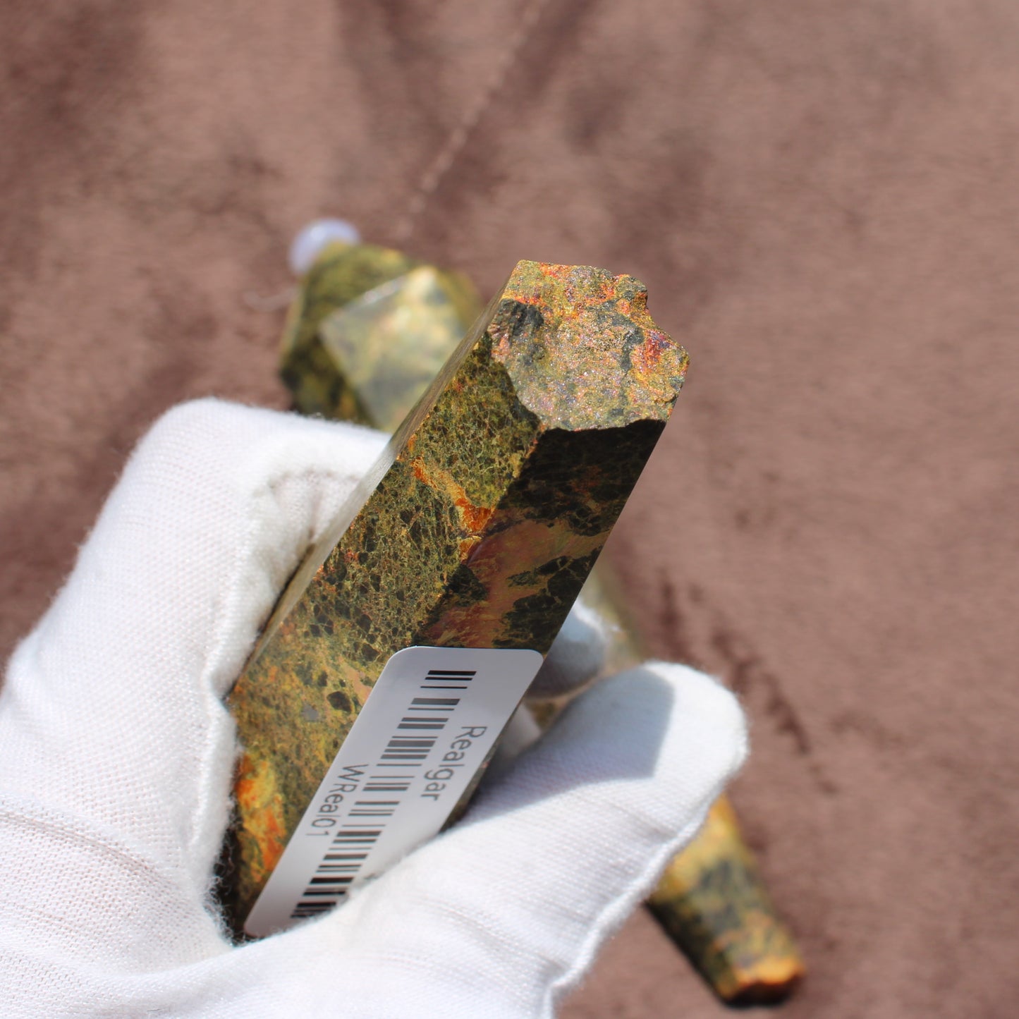 Realgar Wand crystal held in white glove by Different Branches LLC showing orange and green natural mineral textures