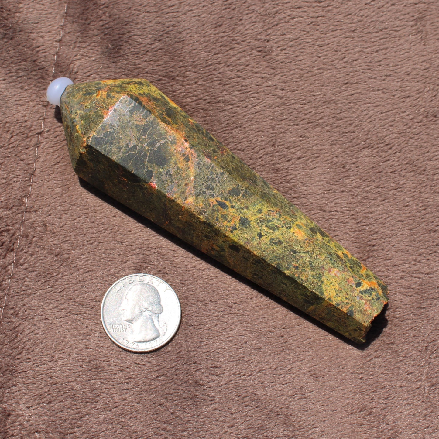 Realgar Wand crystal from Different Branches LLC with green and orange hues placed next to a quarter for size comparison