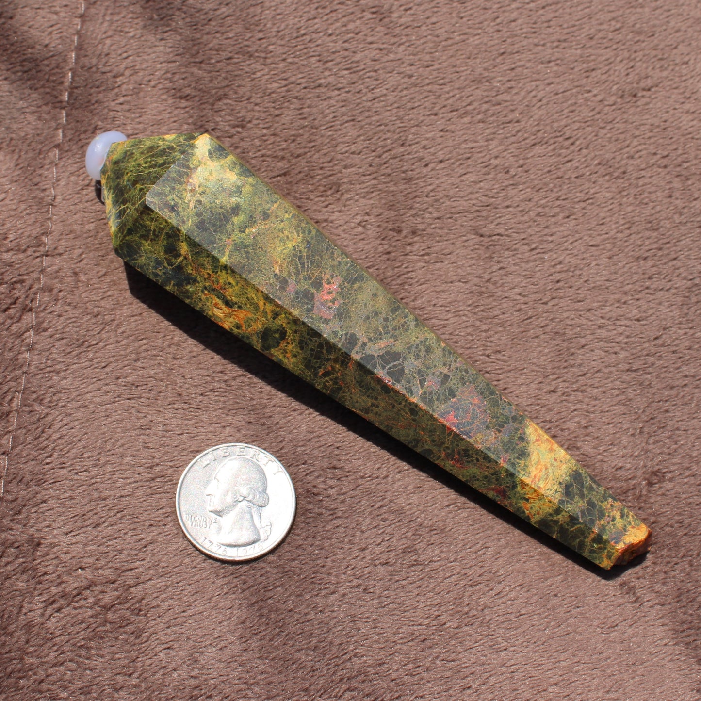 Realgar Wand crystal with mixed green and orange hues displayed next to a quarter for size comparison