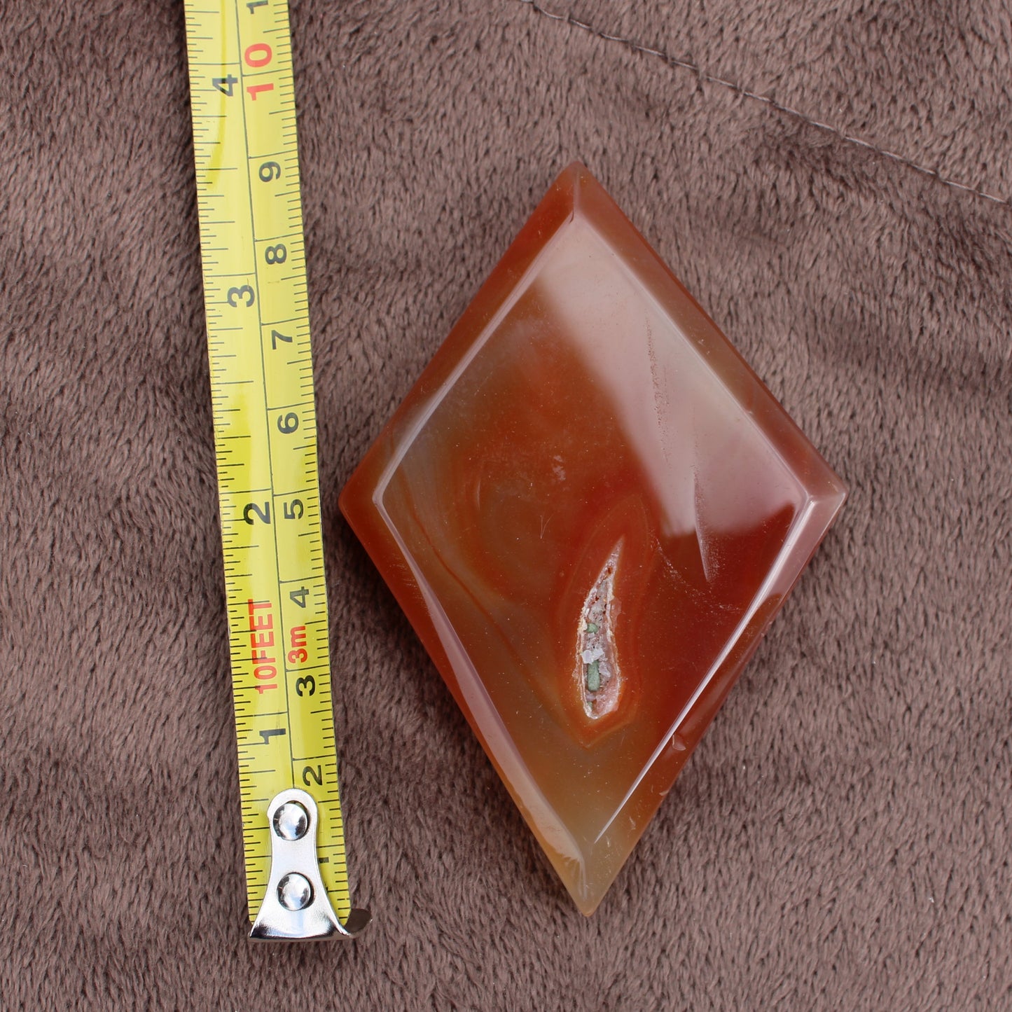 Red Agate Diamond crystal from Different Branches LLC shown next to measuring tape on brown fabric