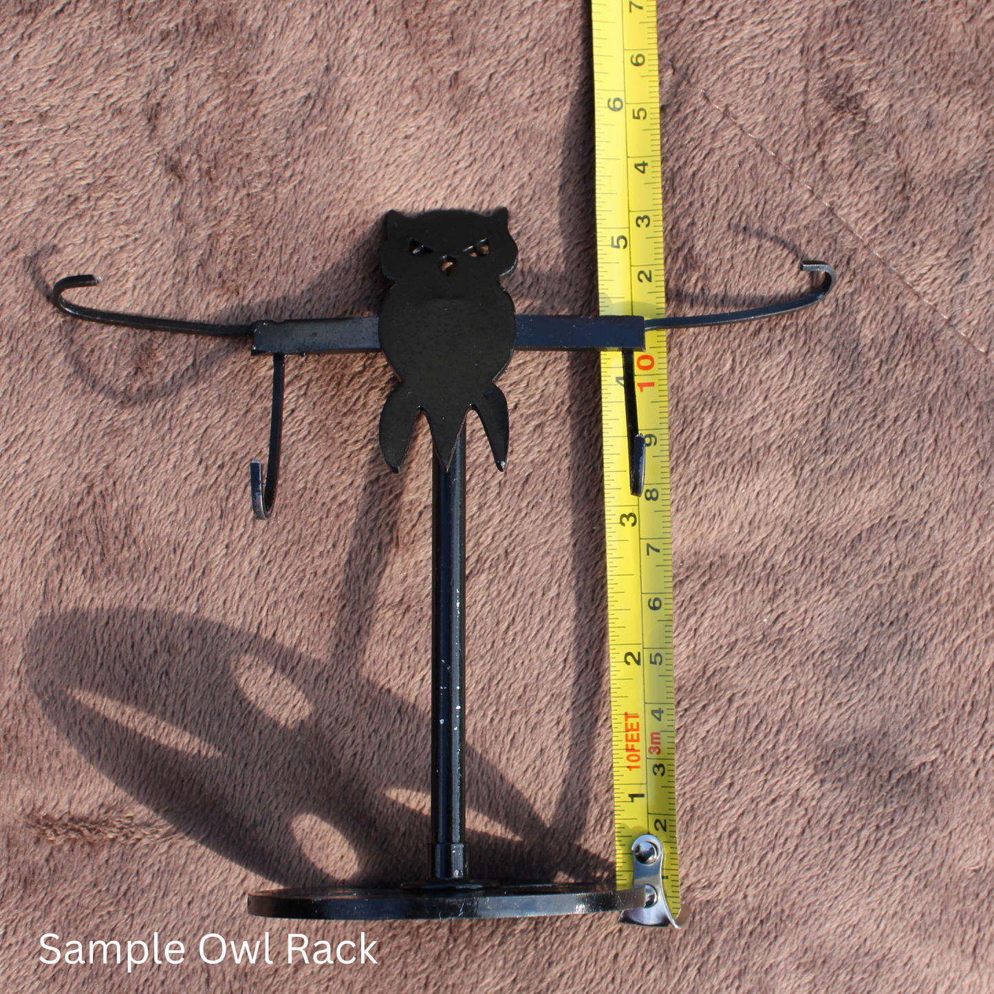 Black metal owl-shaped rack standing next to measuring tape on brown fabric background