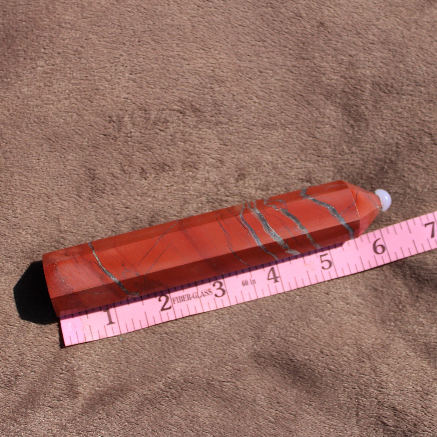 Red jasper tower crystal with unique striations displayed next to a ruler for size reference