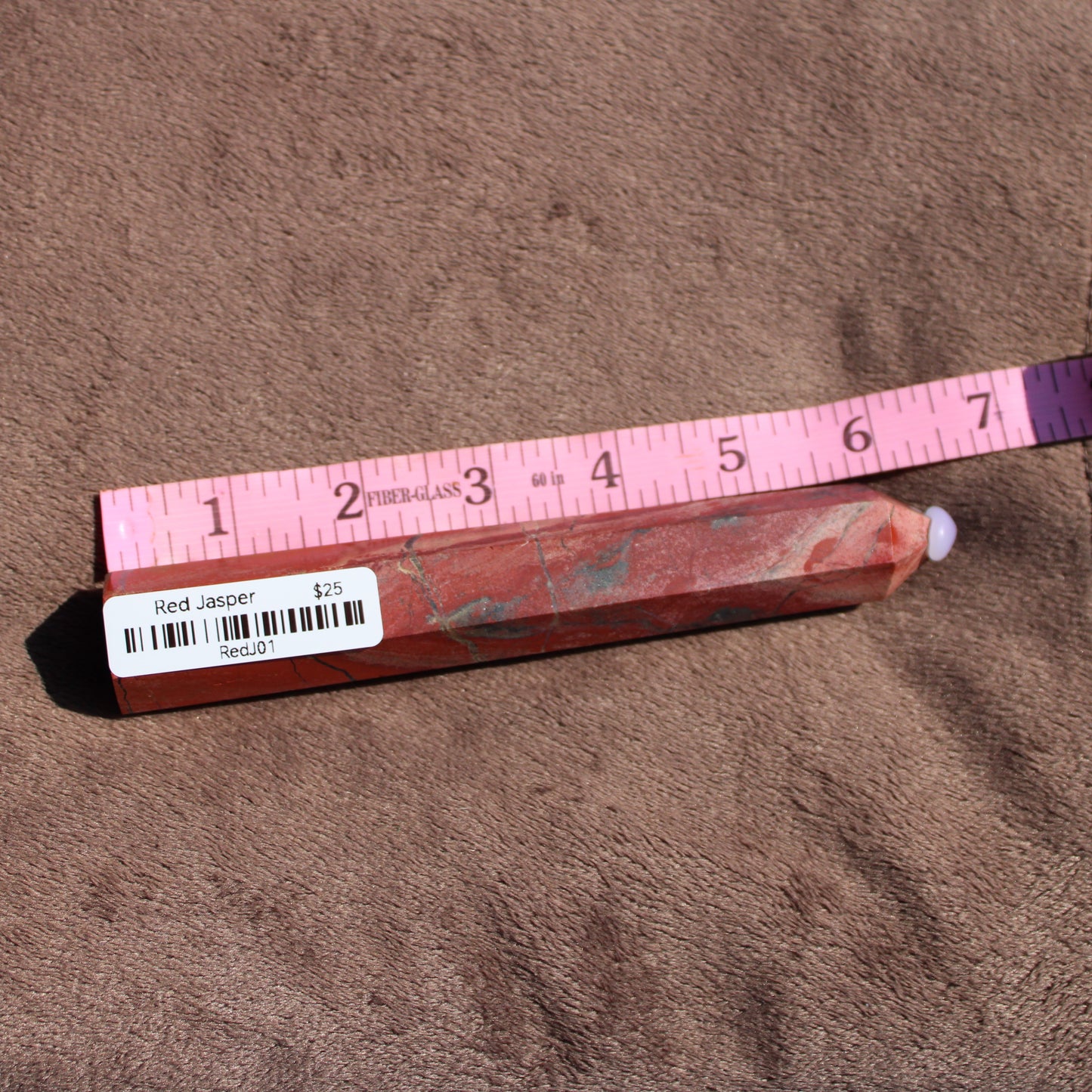 Red jasper tower displayed with a ruler for size reference showcasing its vibrant color and natural texture